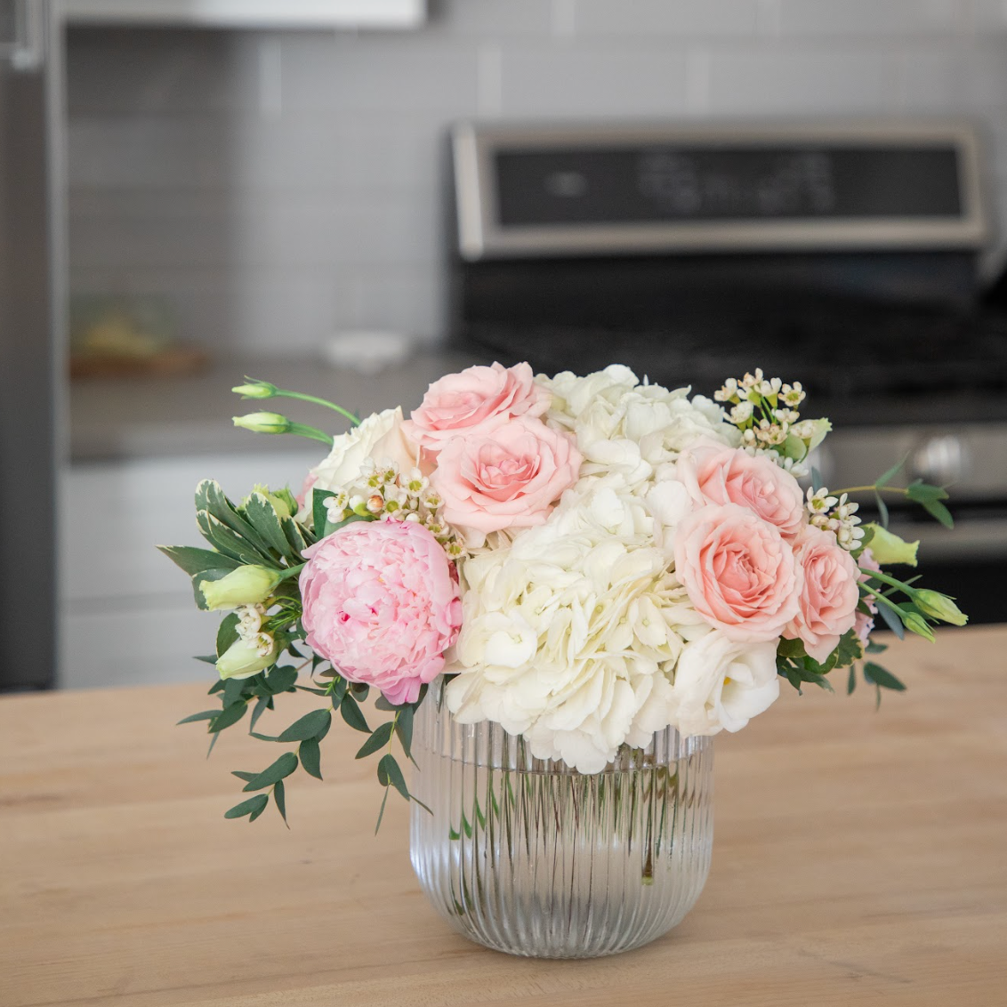 Arrangement of pink and white flowers from Lovebird Flowers in a clear vase on a kitchen counter.