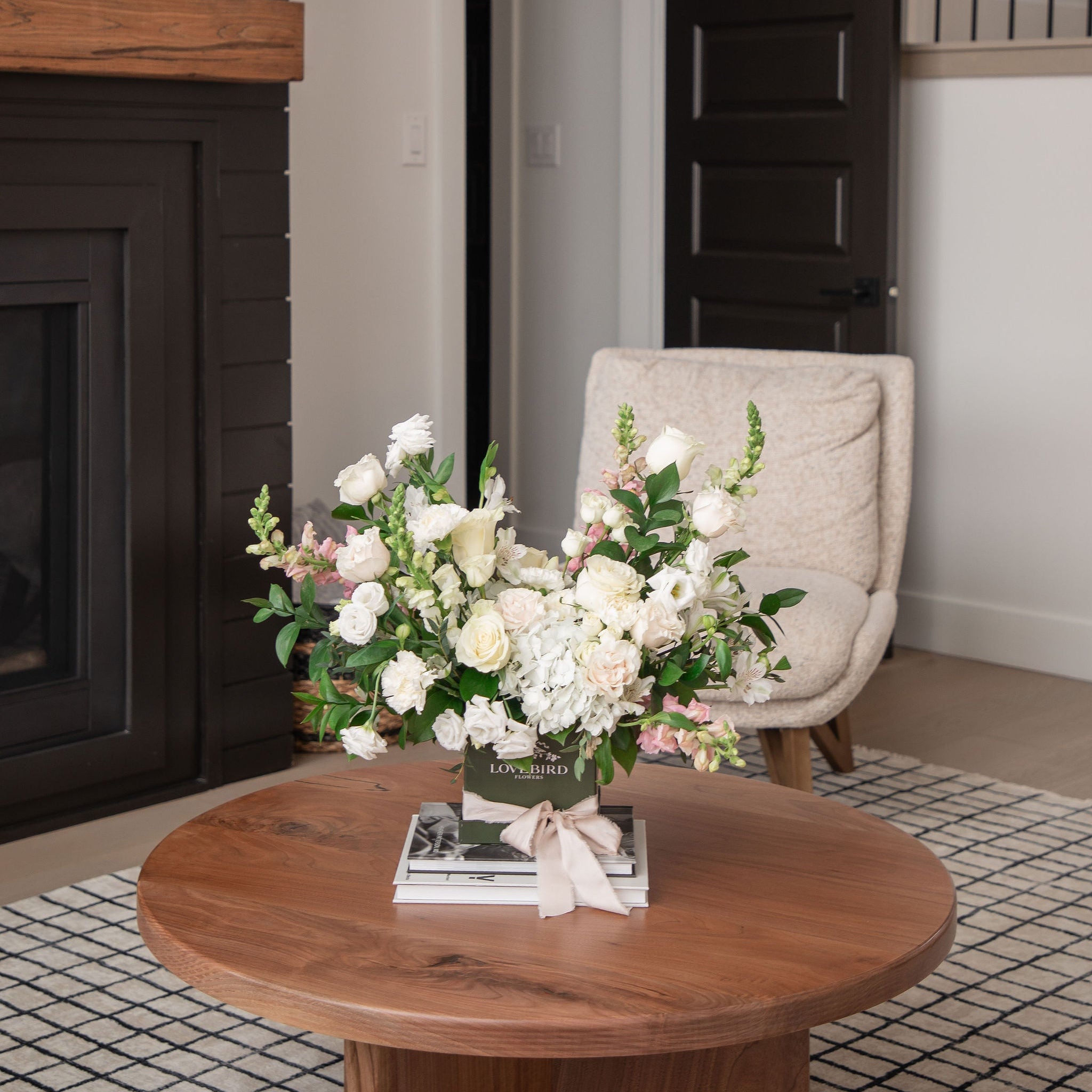 Always & Forever luxury white and blush floral arrangement with hydrangeas and roses in a signature green Lovebird Flowers hat box, displayed on a coffee table.