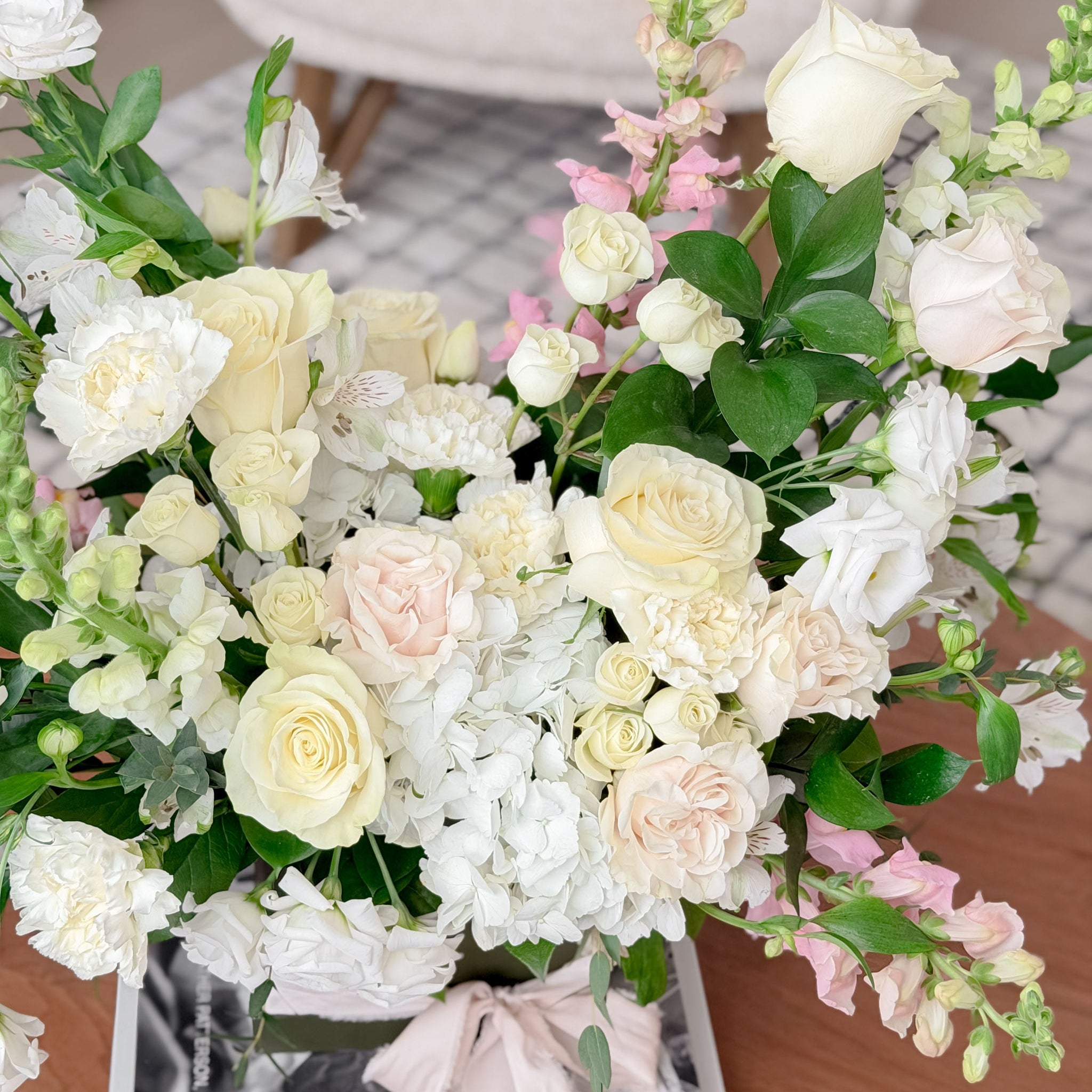 Close-up of the Always & Forever Valentine's arrangement featuring white roses, hydrangeas, and blush pink blooms from Lovebird Flowers in London, Ontario on a wood coffee table