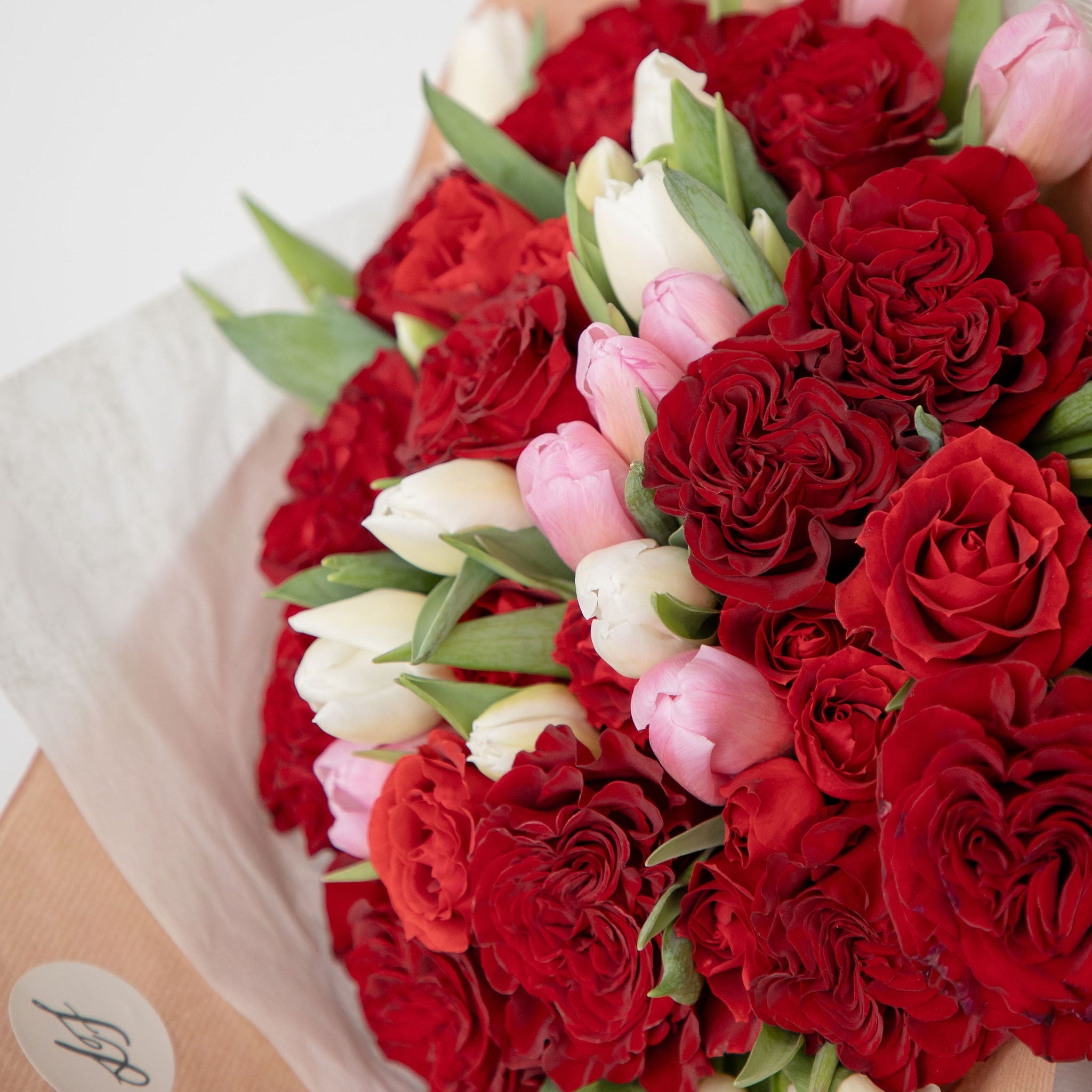 Bouquet of red roses and pink tulips wrapped in brown paper with a white label.