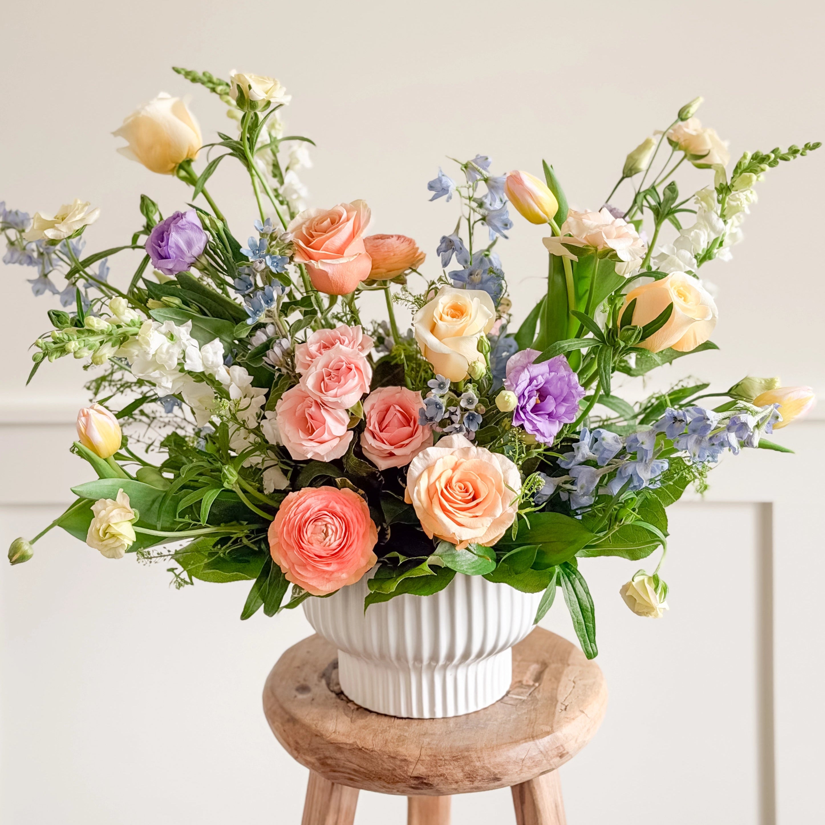 Bouquet of flowers in a white vase on a wooden stool against a light background