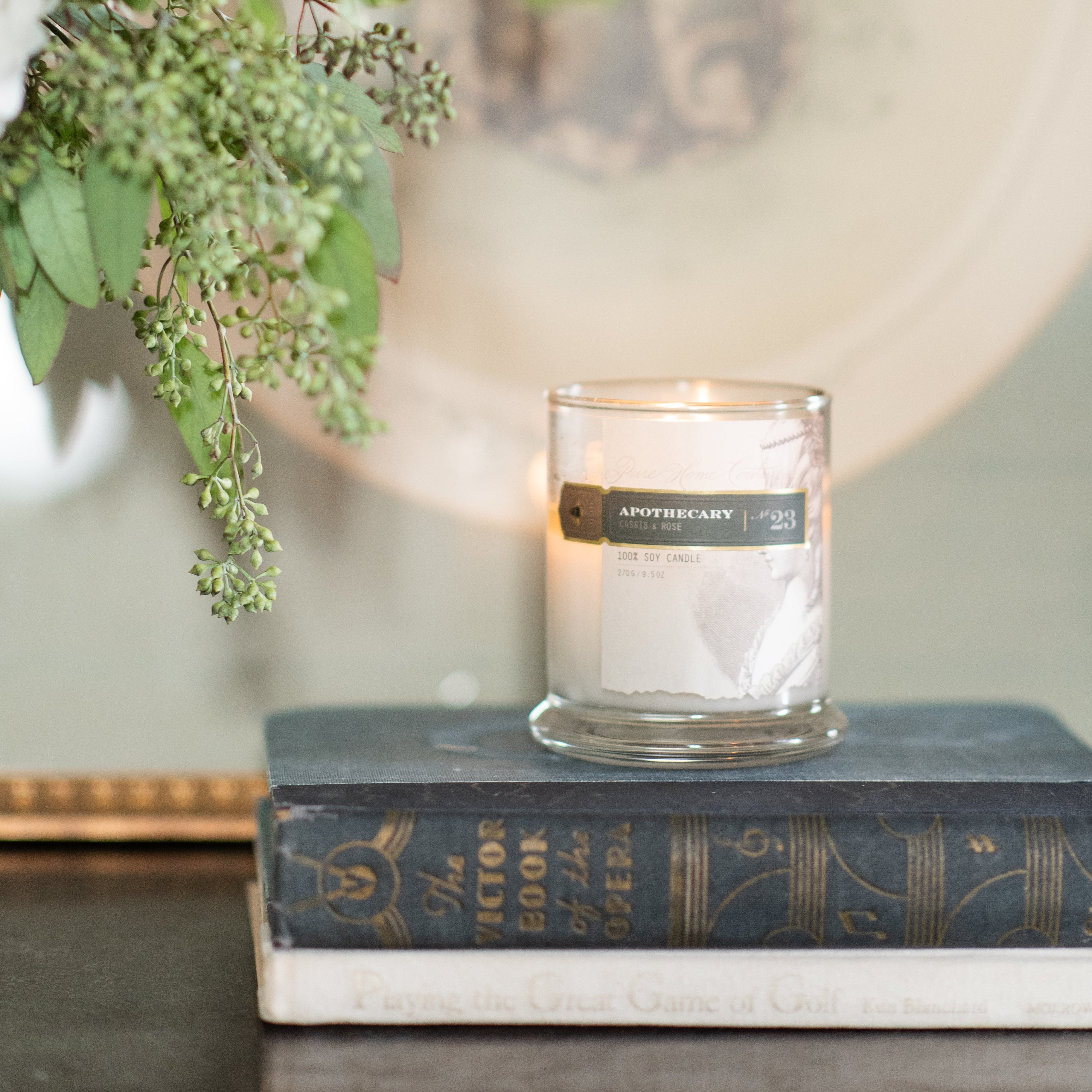 Pure Home Apothecary Candle in a glass holder on a book with flowers in the background