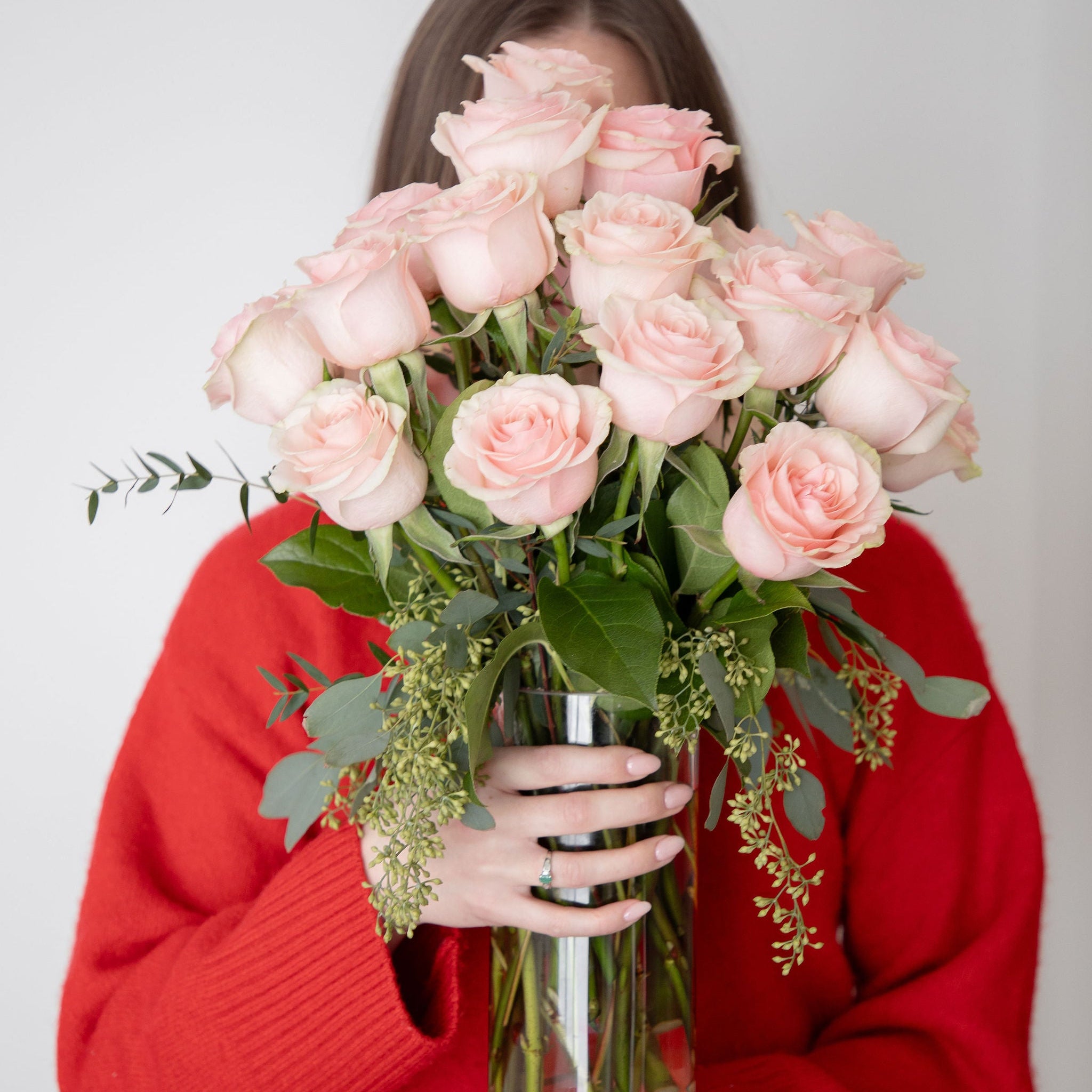 Person wearing a red sweater holding a bouquet of pink roses against a plain background