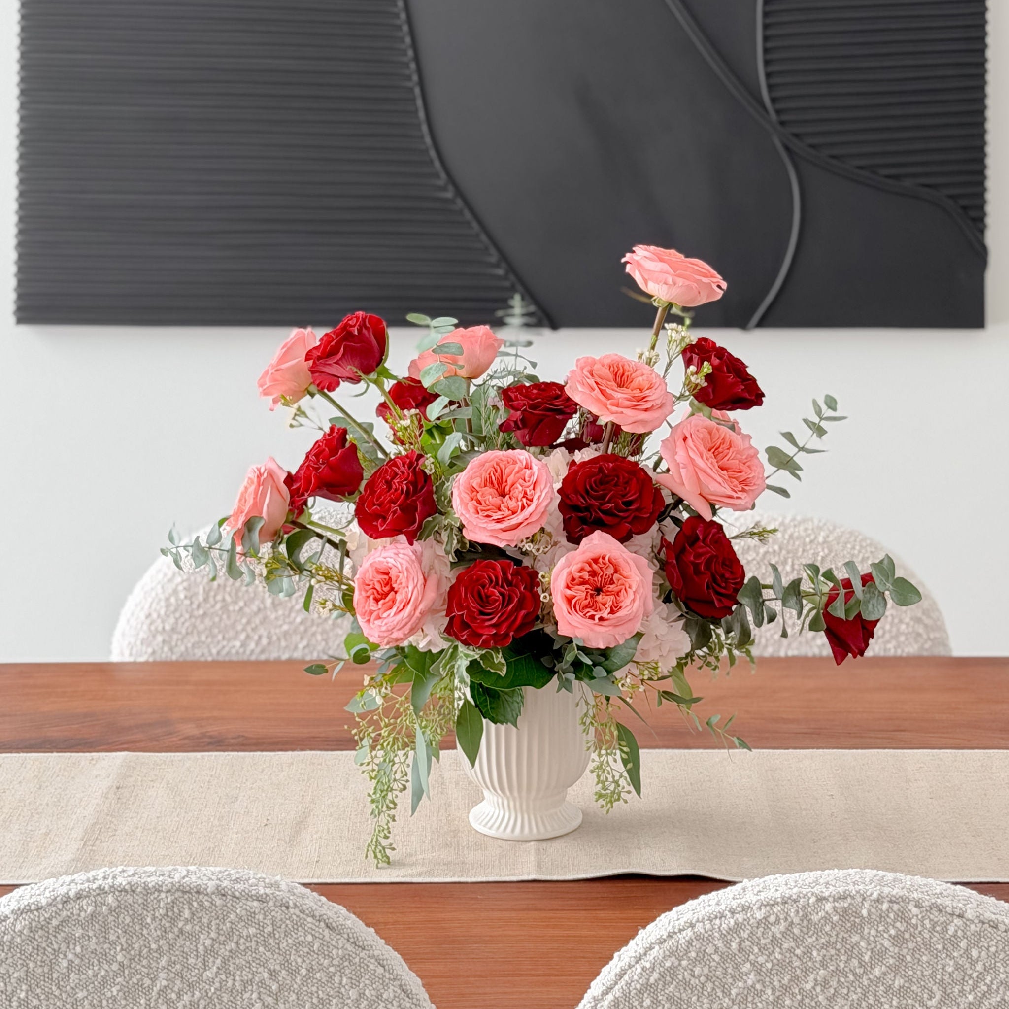 Floral arrangement in a white vase on a dining table with a gray wall in the background