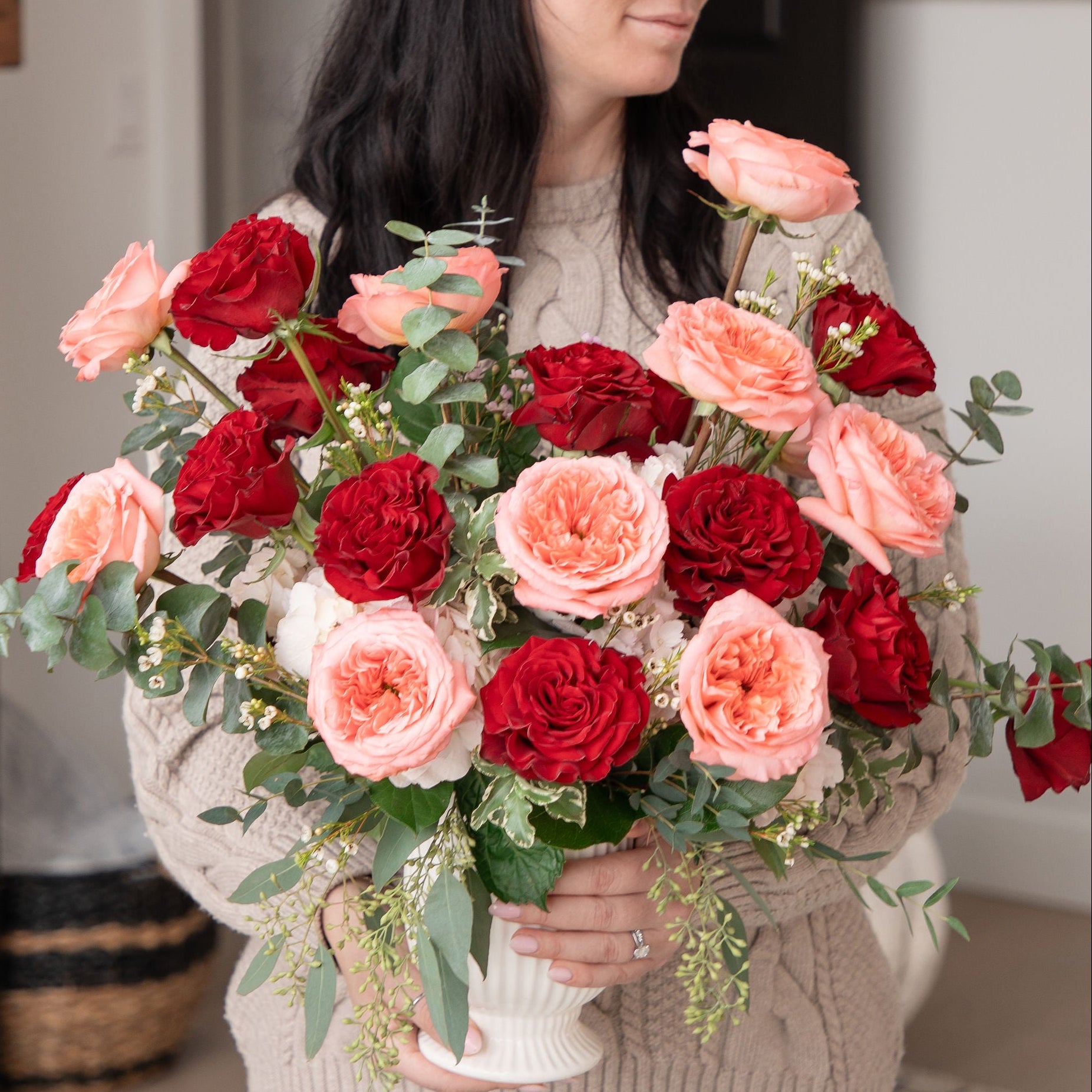 Woman holding a large bouquet of red and pink roses indoors.