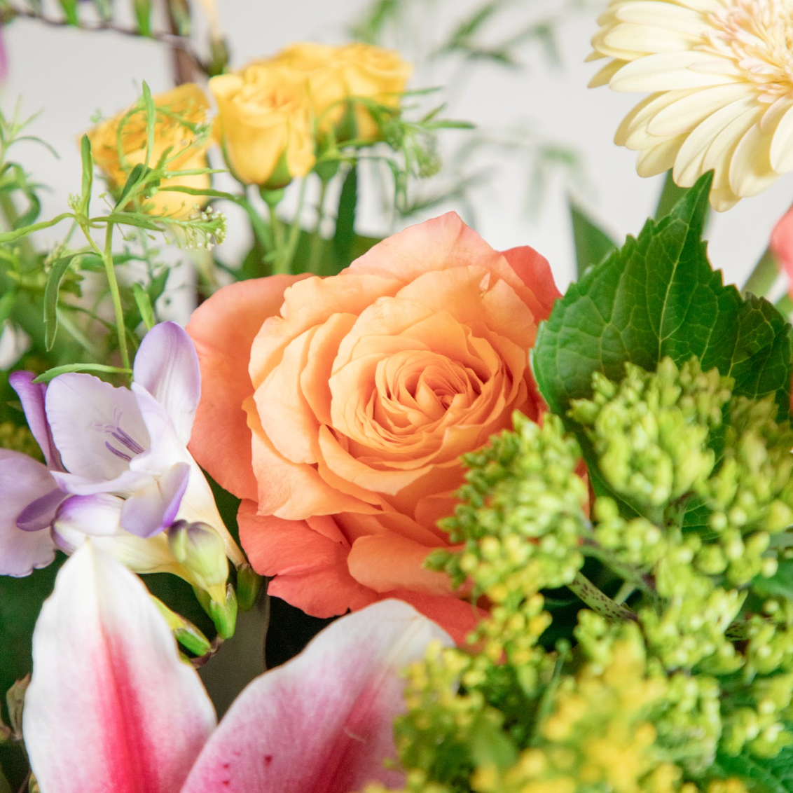 Close-up of a bouquet of flowers with peach roses, yellow tulips, and greenery.