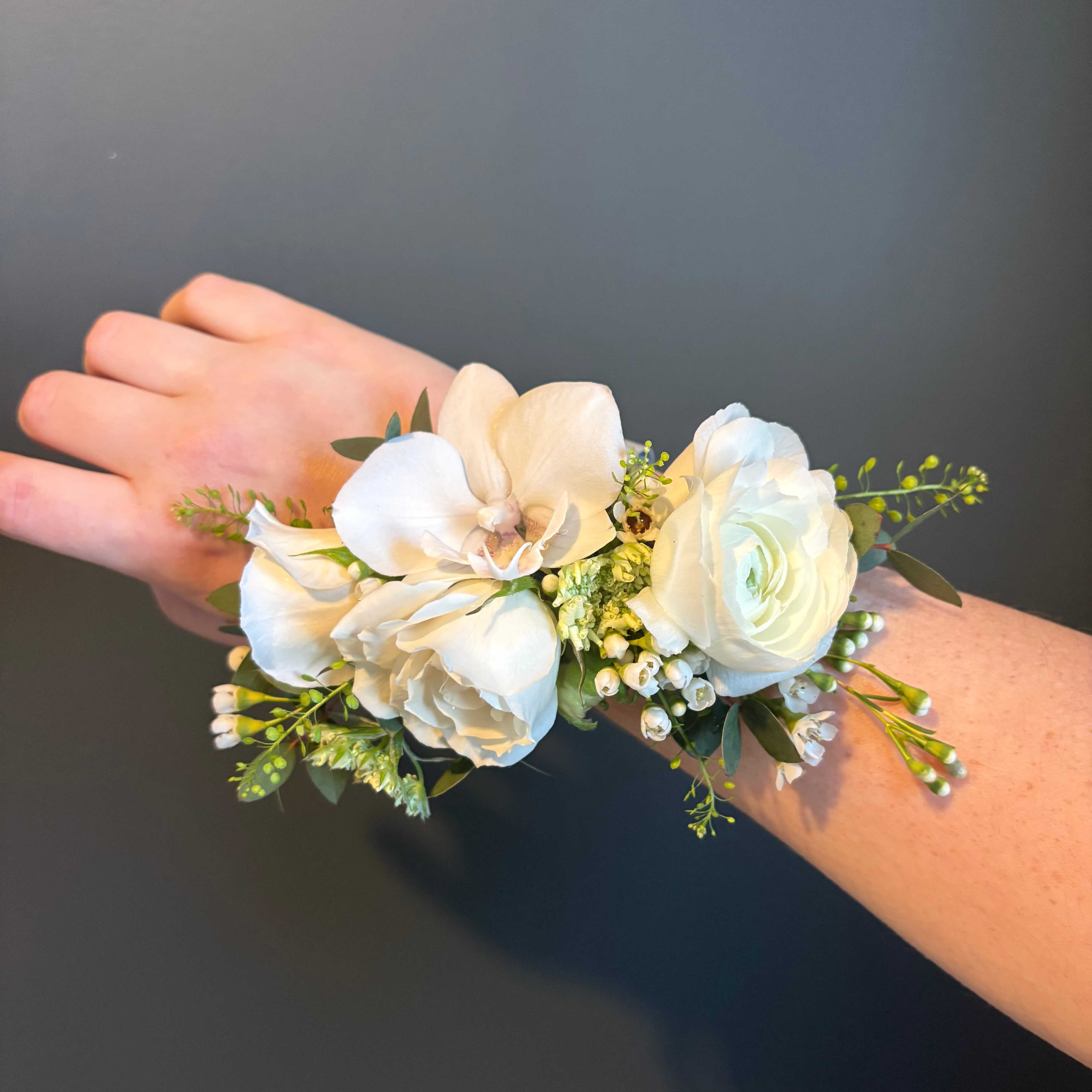 Floral wrist corsage on a person's wrist against a dark background