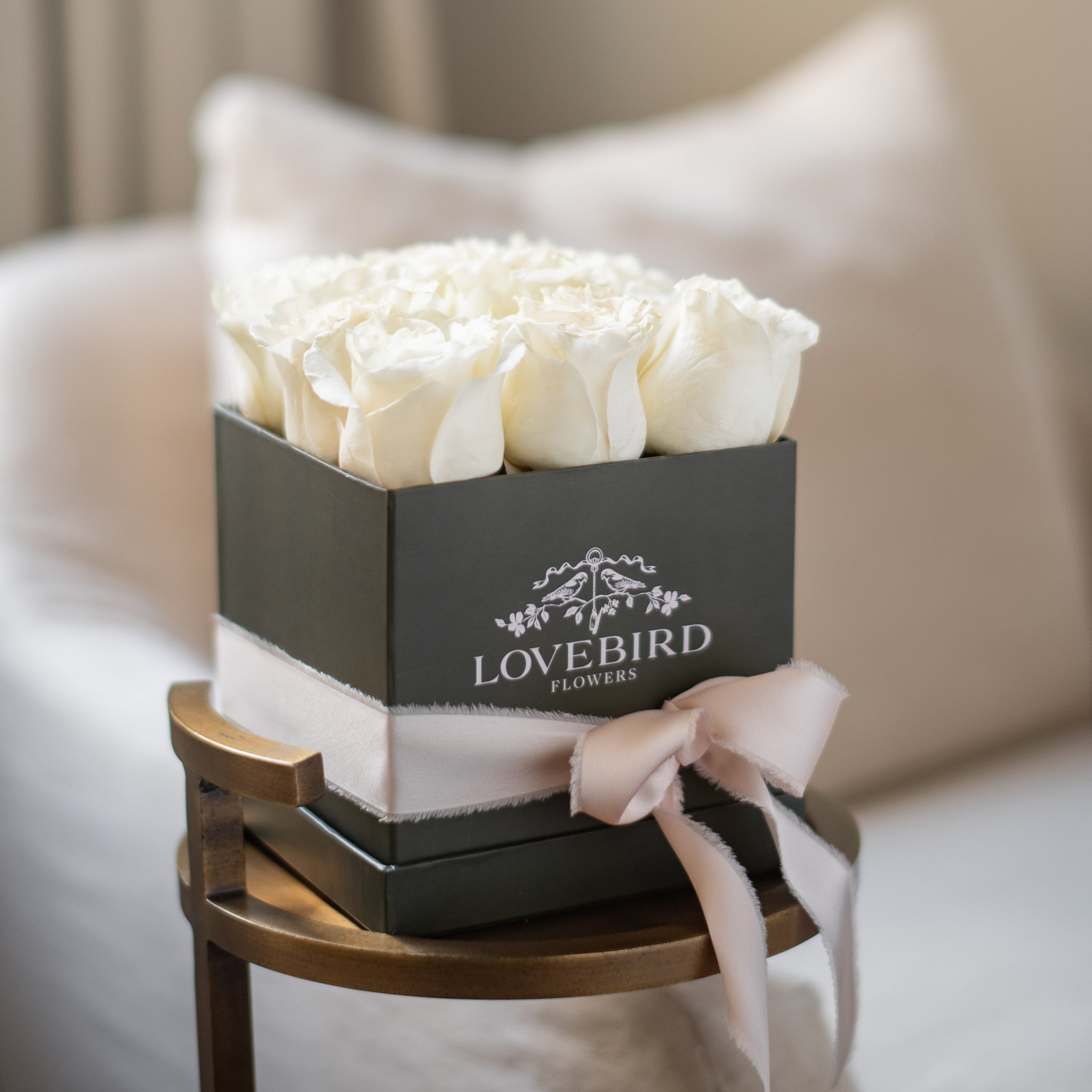 Box of white roses with 'Lovebird Flowers' branding on a wooden stand.
