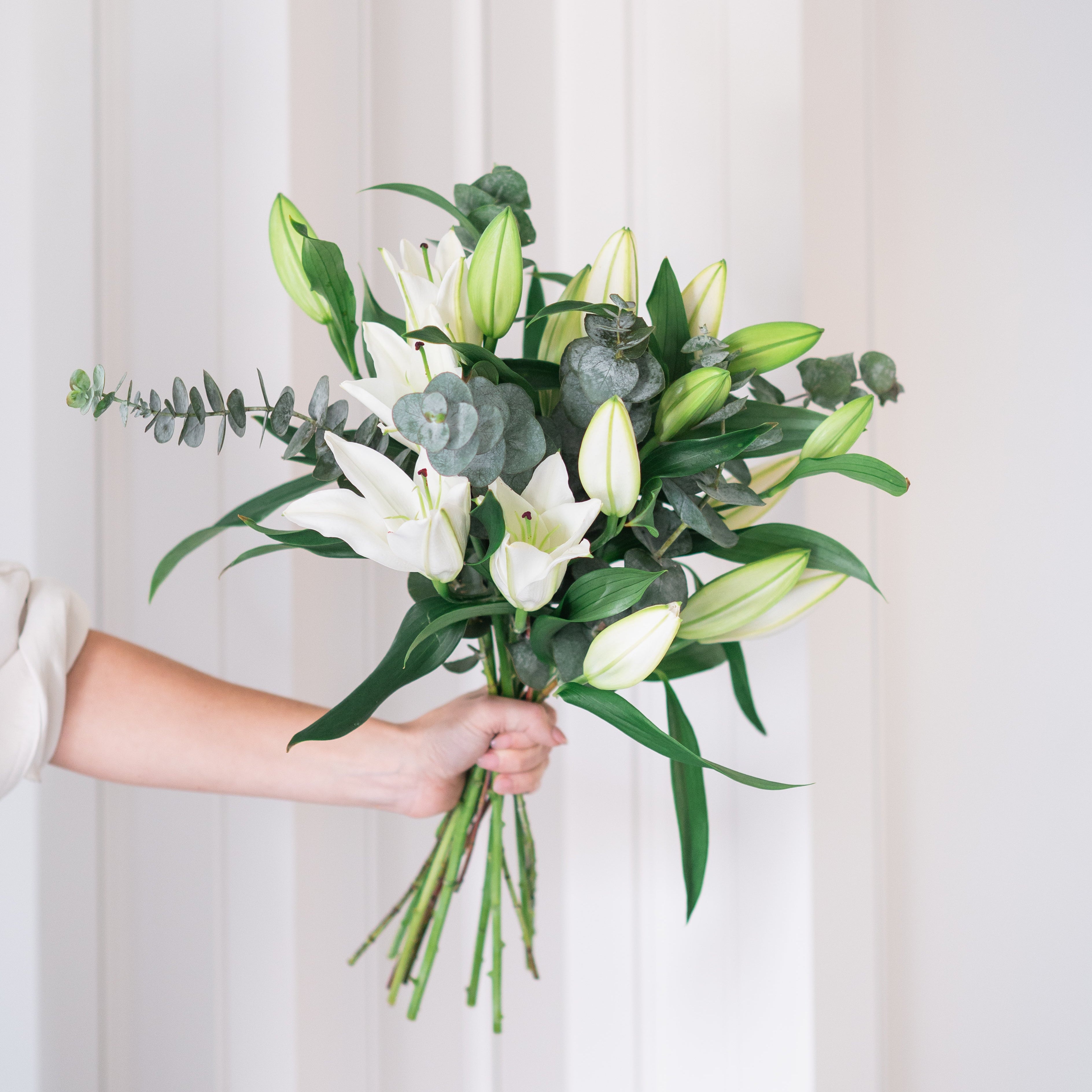 Bouquet of white lilies and greenery held by a person against a white background