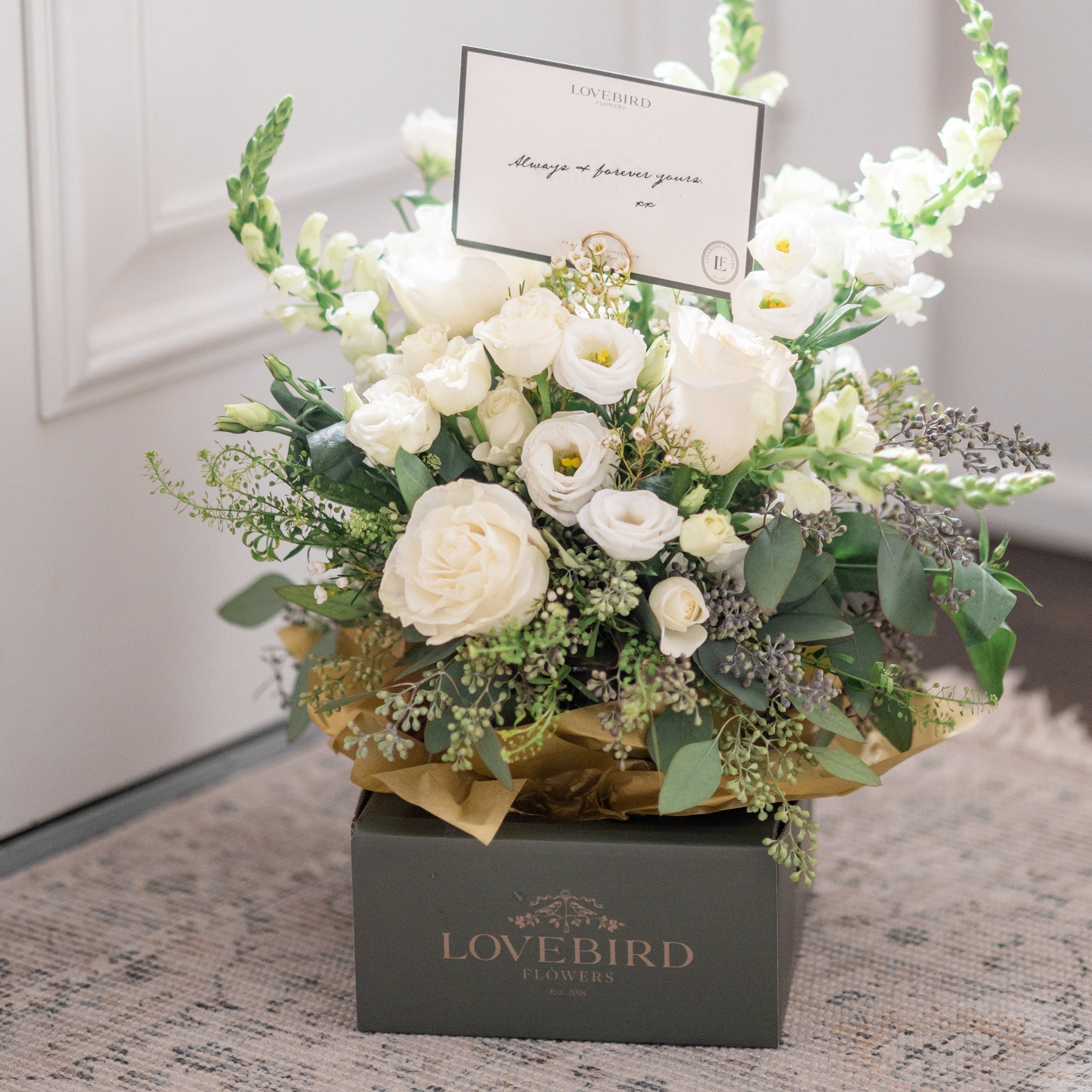 White floral arrangement in a Lovebird Flowers delivery box with a card.