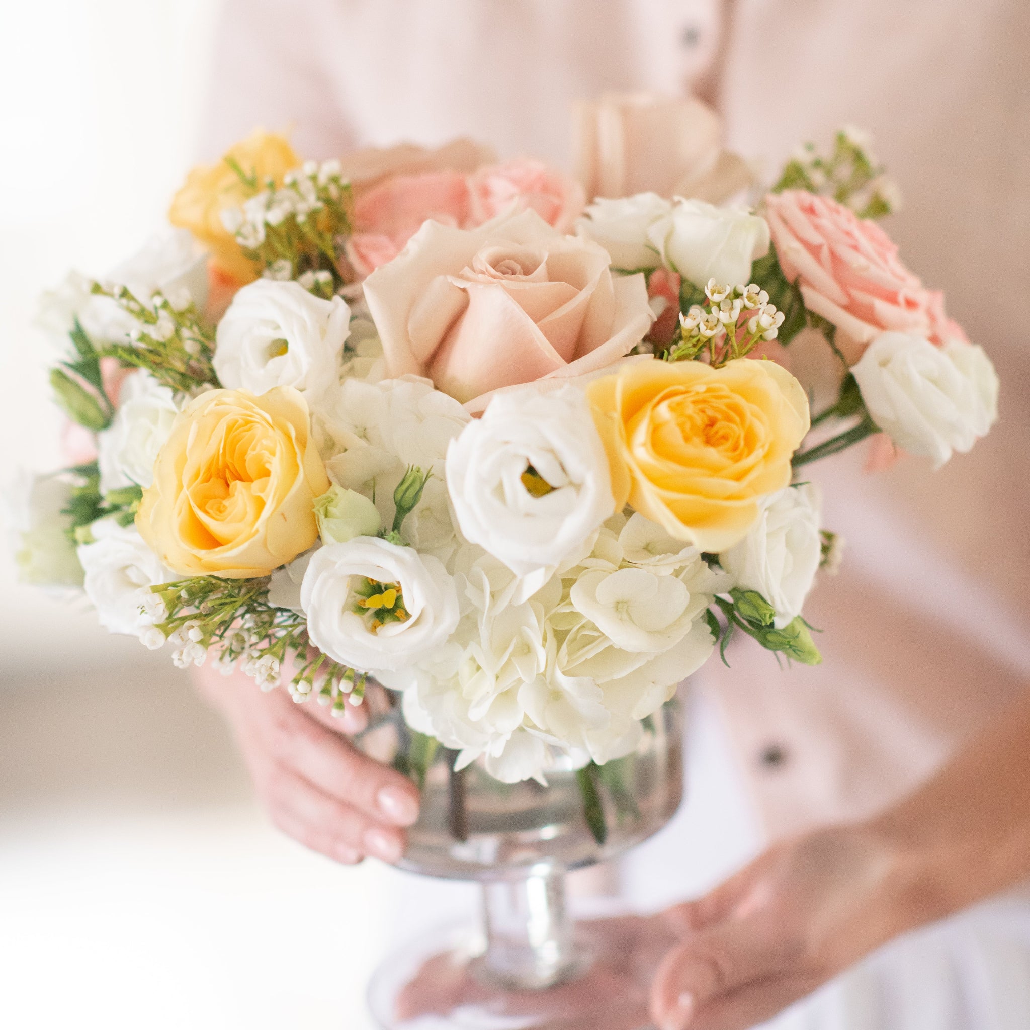 pastel yellow and blush roses with white hydrangea and fluffy white lisianthus being held by a woman in pink