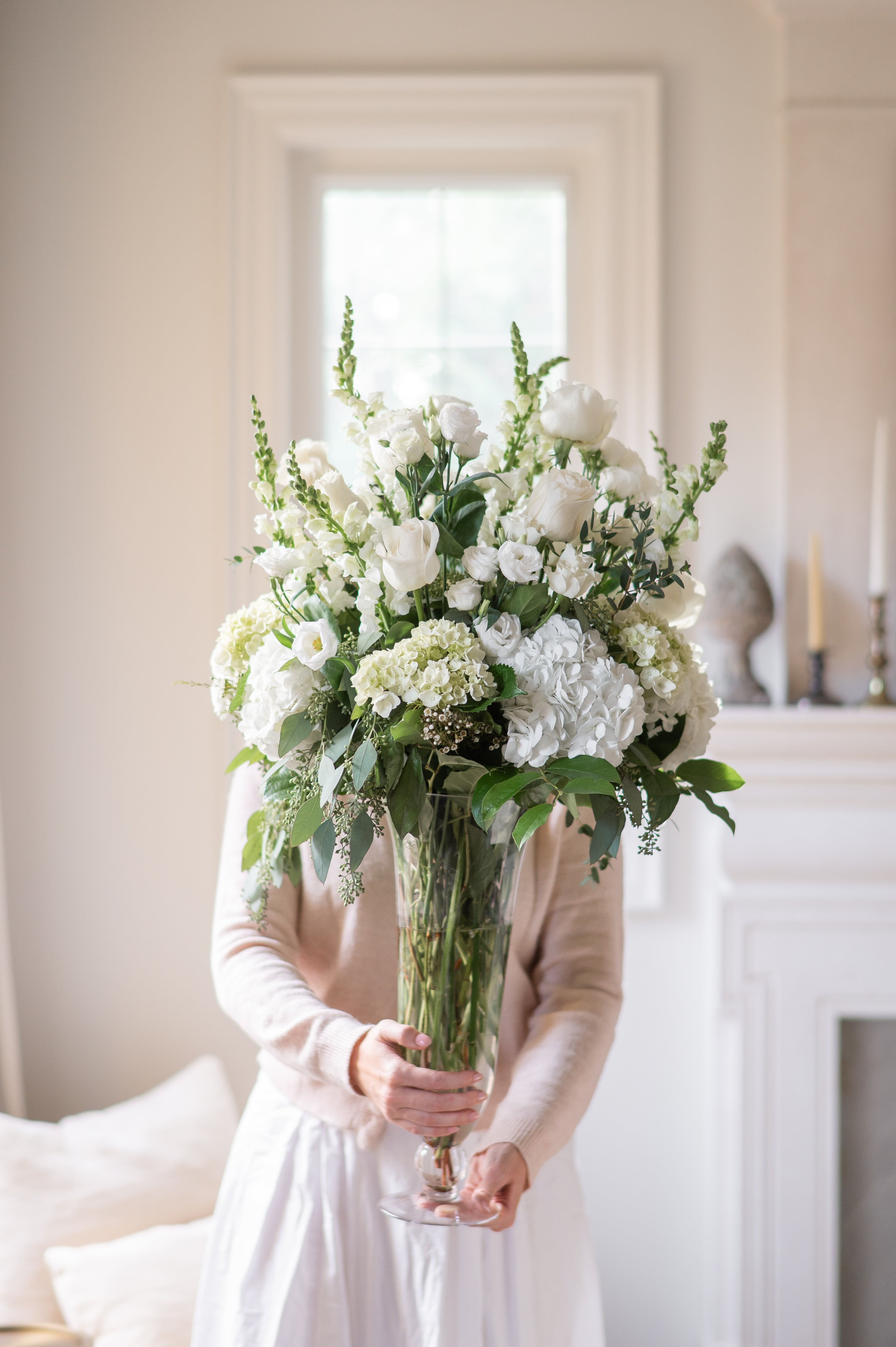 Person holding a large bouquet of white and green flowers in a room with a fireplace.