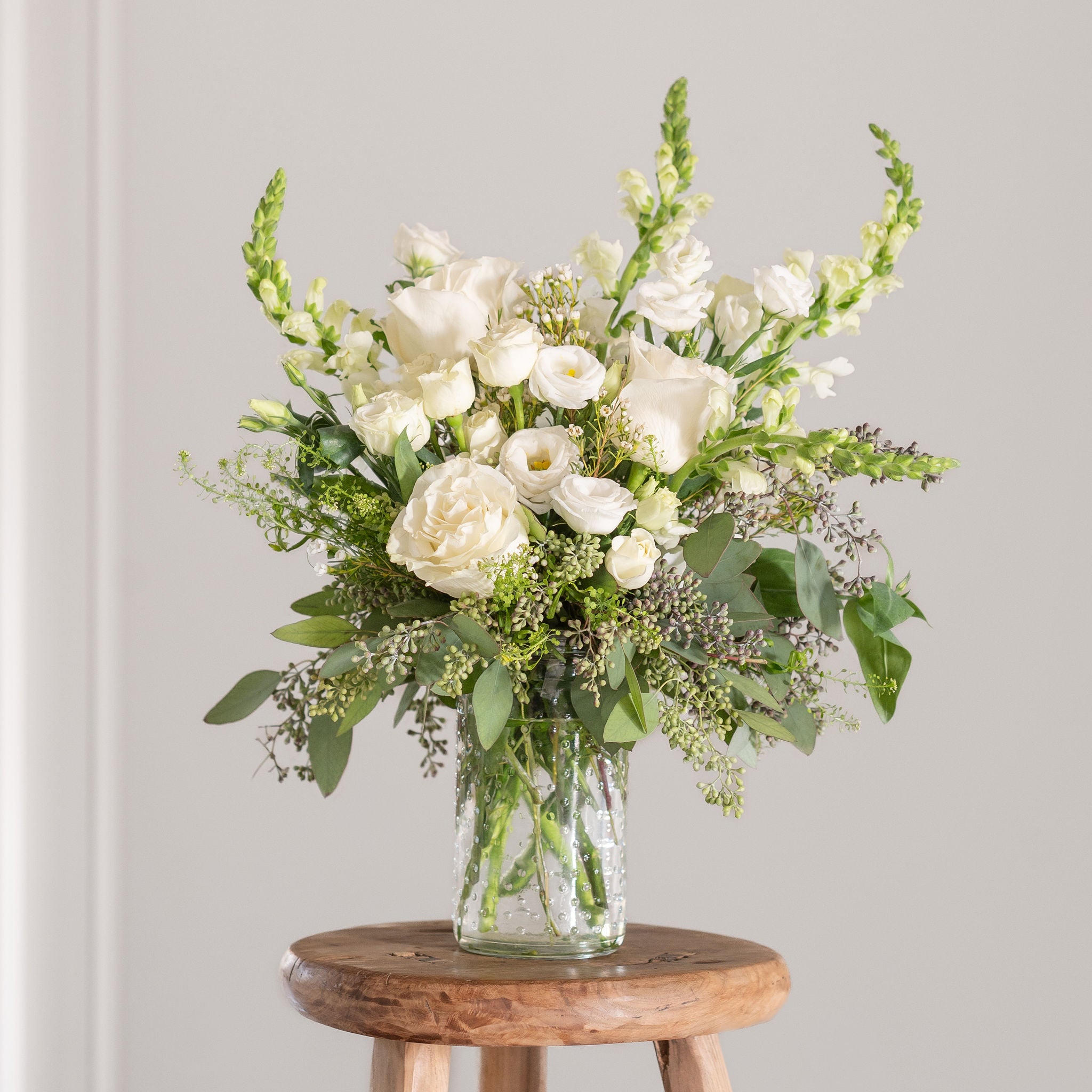 white flower arrangement featuring snap dragons, white lisianthus, spray roses, playa blanca roses, seeded eucalyptus and thilapsi
