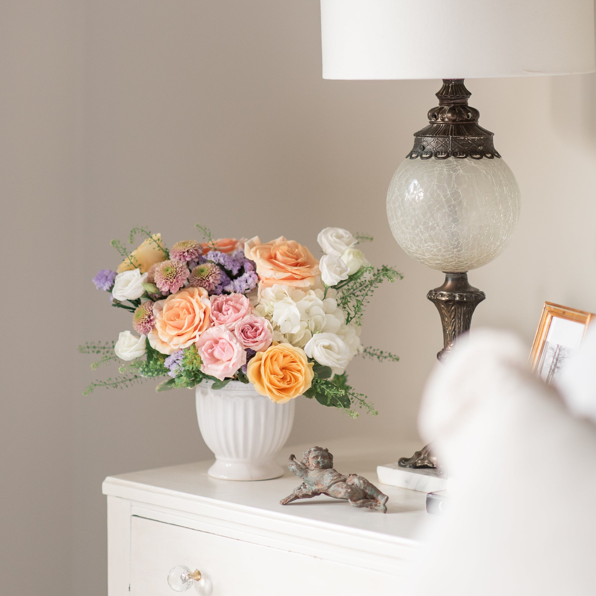 pastel flower arrangement with pink, peach and yellow roses, lavender statice and pink button mums on a dresser