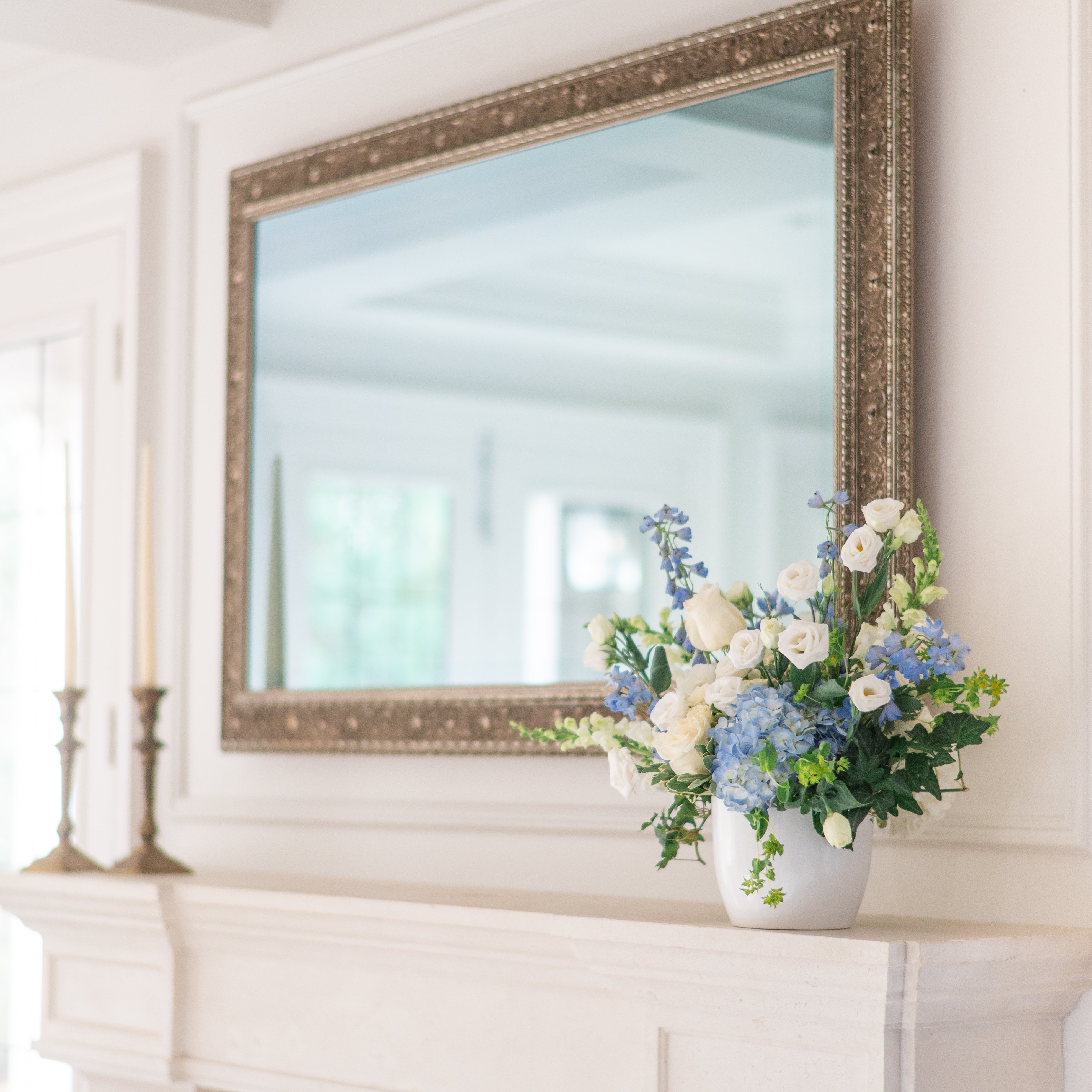 Blue & white floral arrangement with lisianthus, snap dragons and blue hydrangea on a fireplace mantel with a mirror above