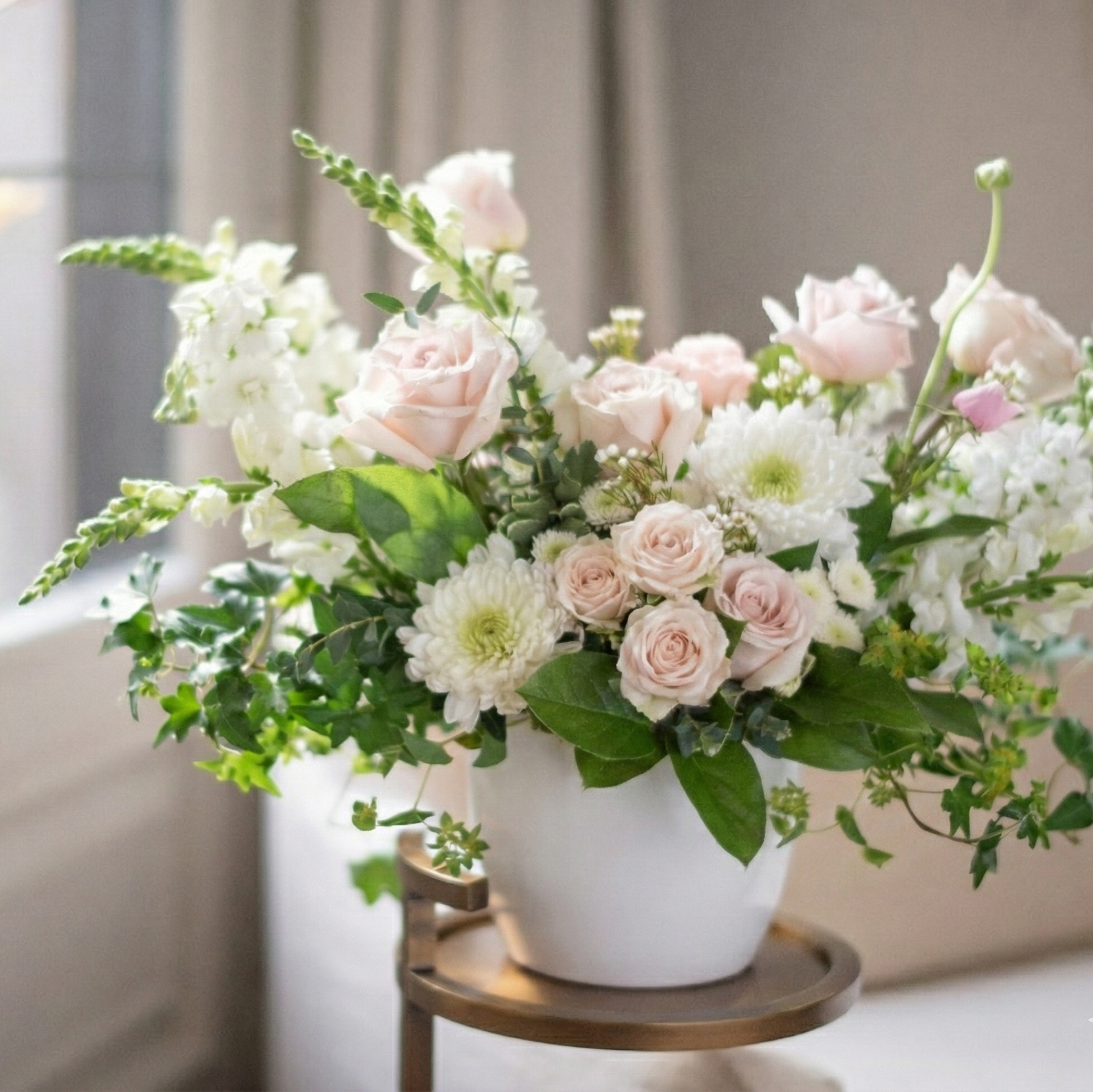 Floral arrangement in a white vase on a small wooden table with a neutral background.