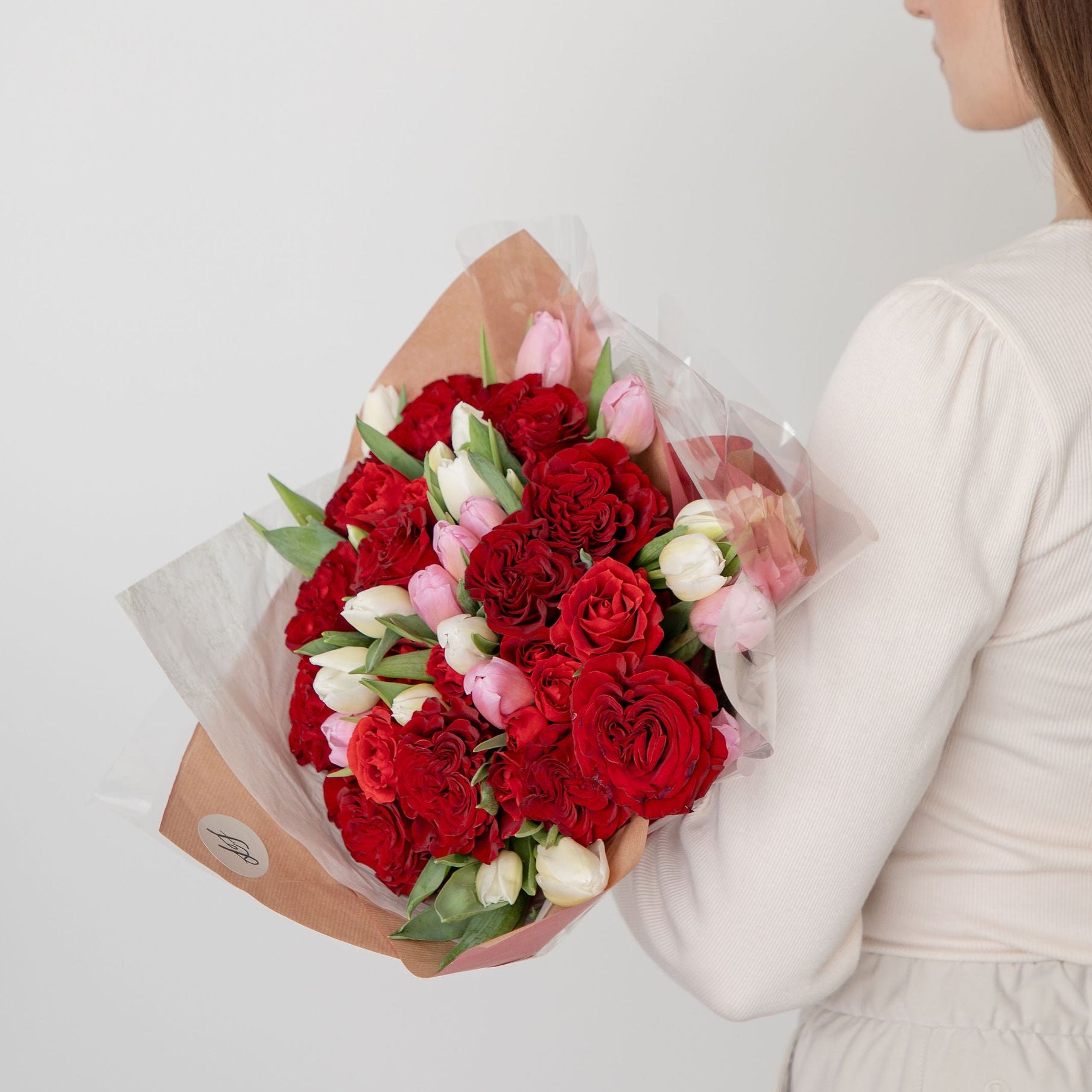 Woman holding a bouquet of red hear roses and pink and white ultips against a white background
