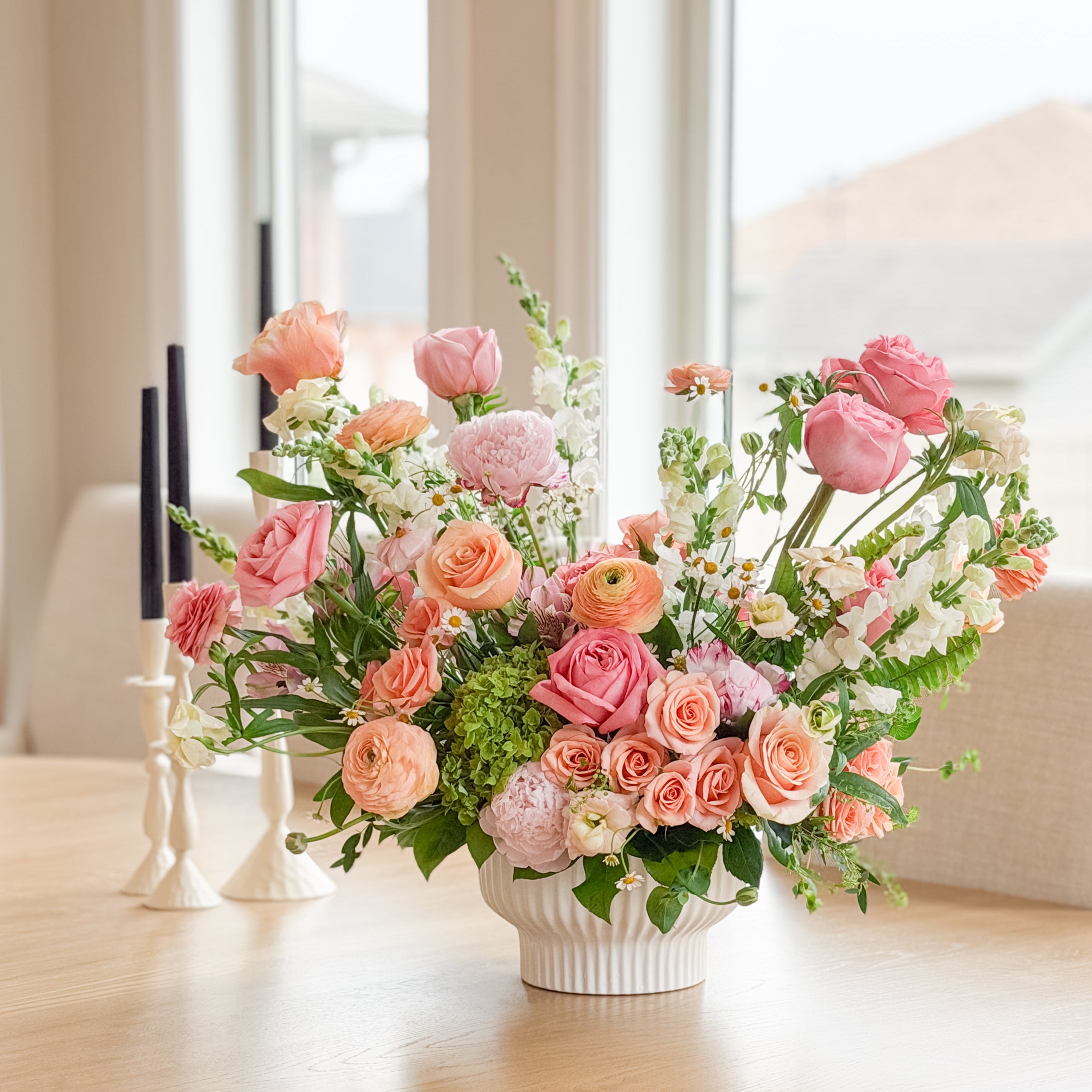 Floral arrangement on a wooden table with candles in the background