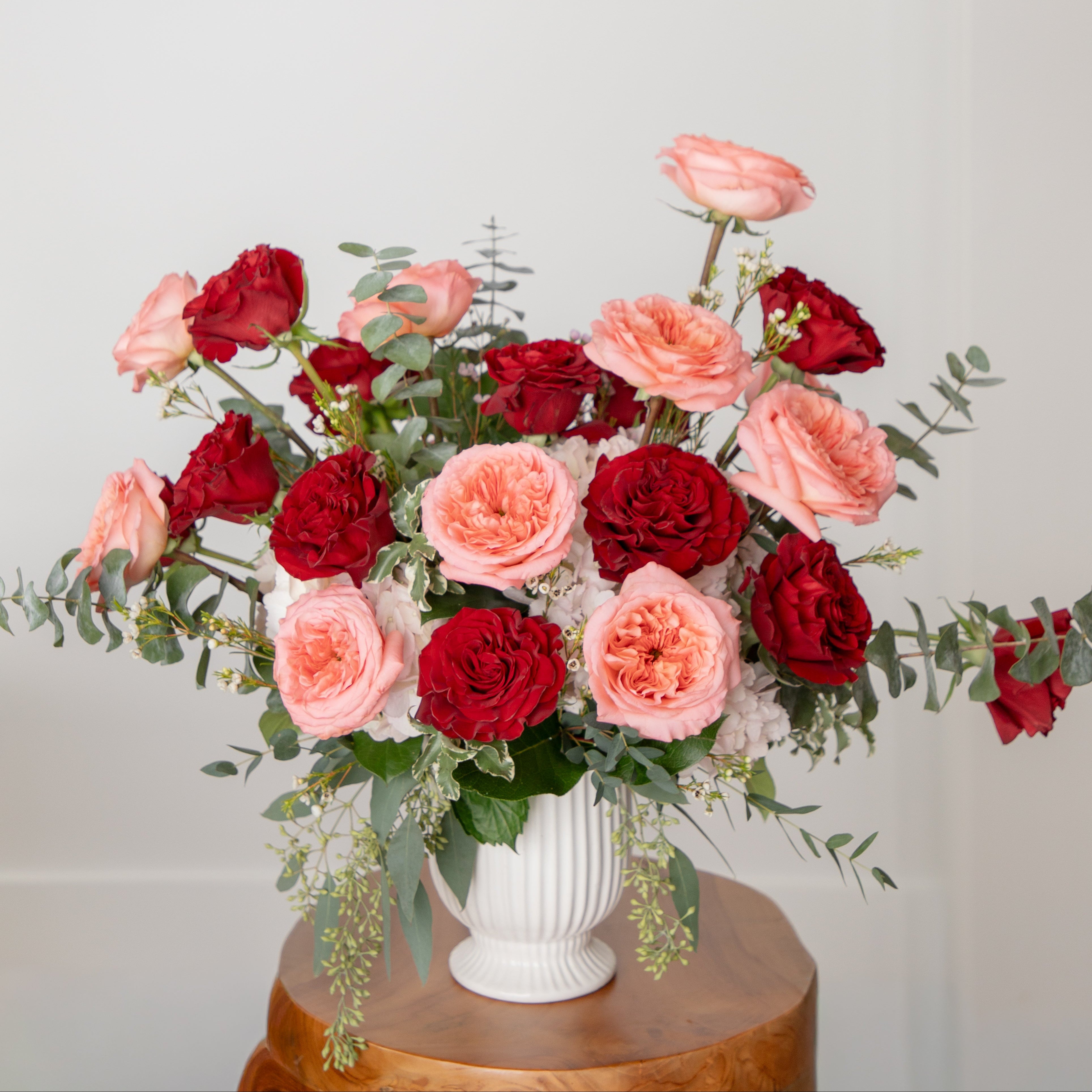 Valentine's arrangement of red and pink flowers in a white vase on a wooden surface with a light gray background from Lovebird Flowers