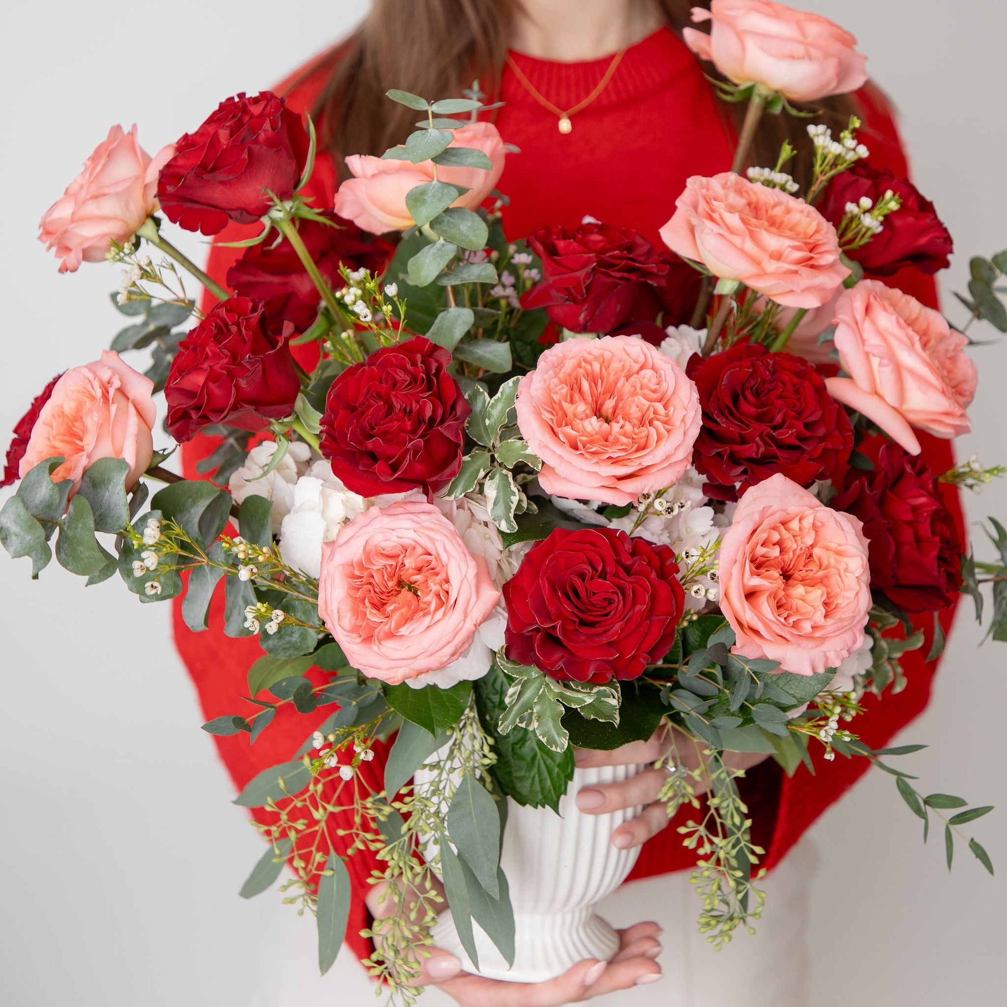 Woman holding a large bouquet of red and pink flowers against a white background