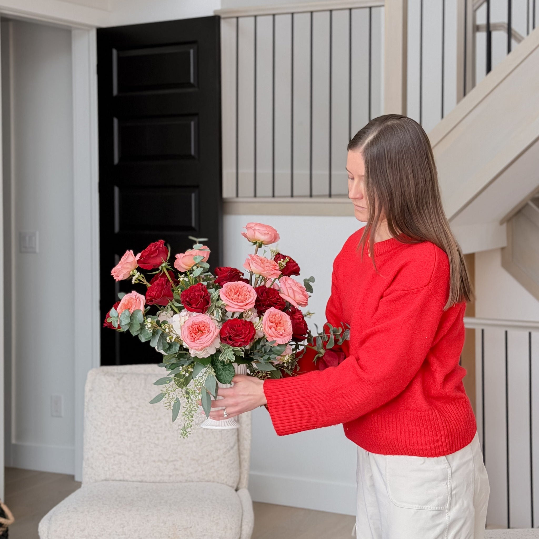 Woman in a red sweater holding a bouquet of flowers in a home setting.
