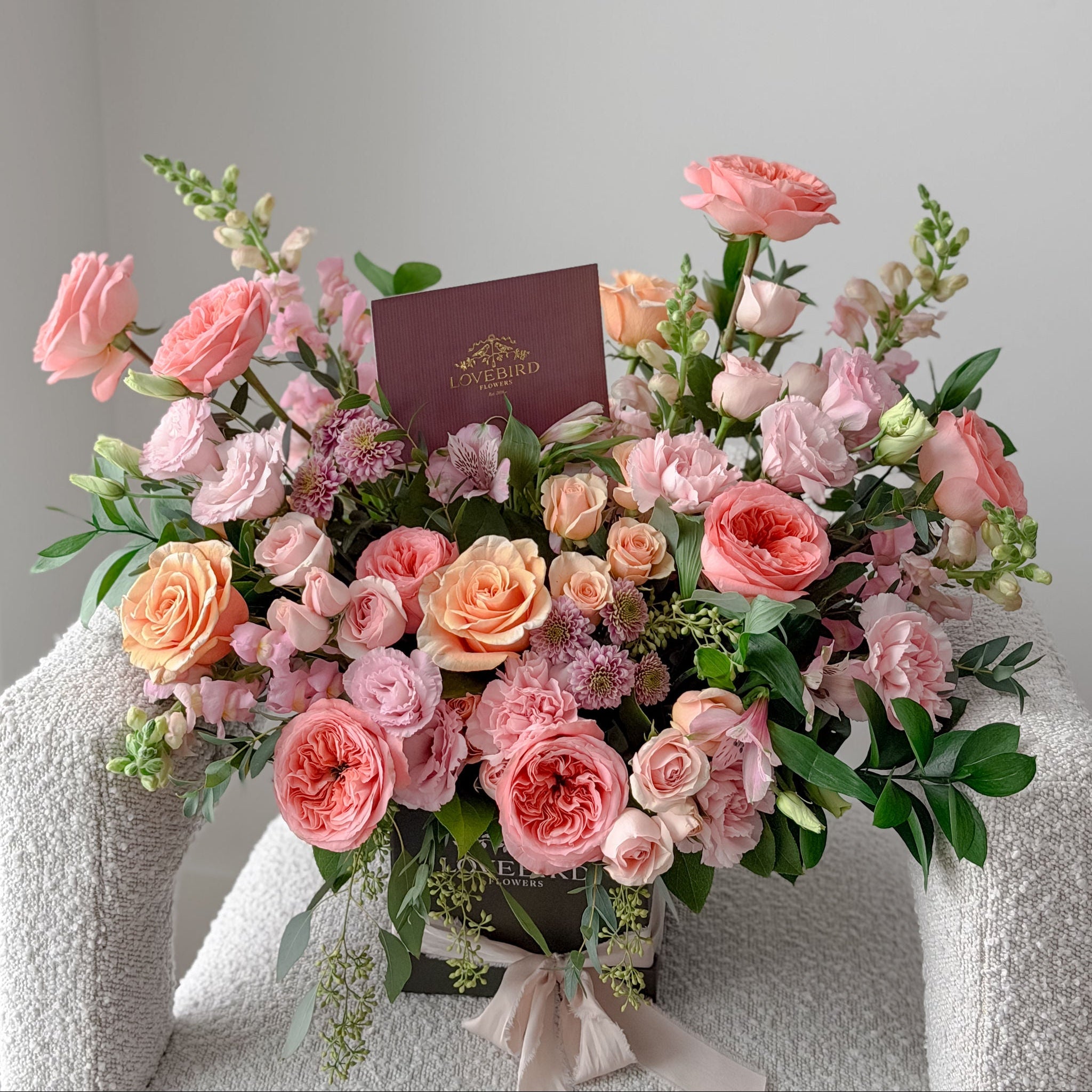 Bouquet of pink and peach roses with a Lovebird Flowers card on a light gray background
