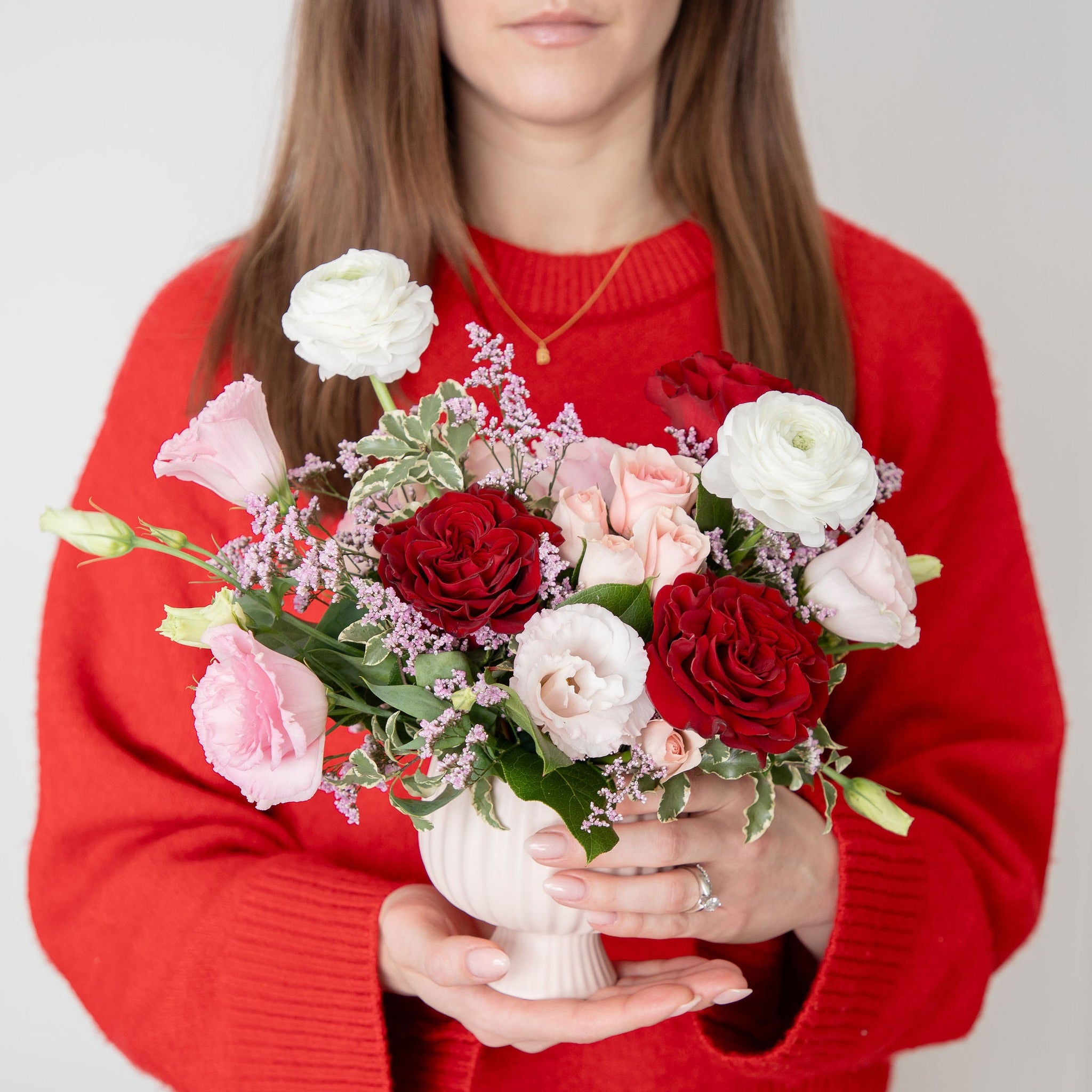 Woman in a red sweater holding two bouquets of flowers against a plain background