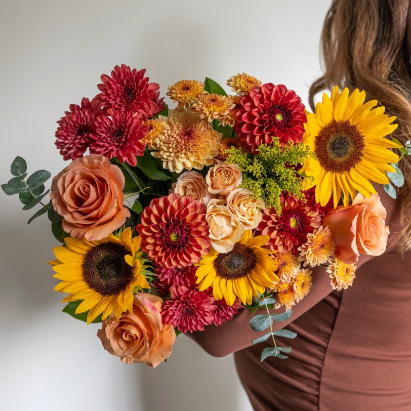 Woman holding a grande, fall inspired bouquet with dahlias, sunflowers, solidago, mums from Lovebird Flowers