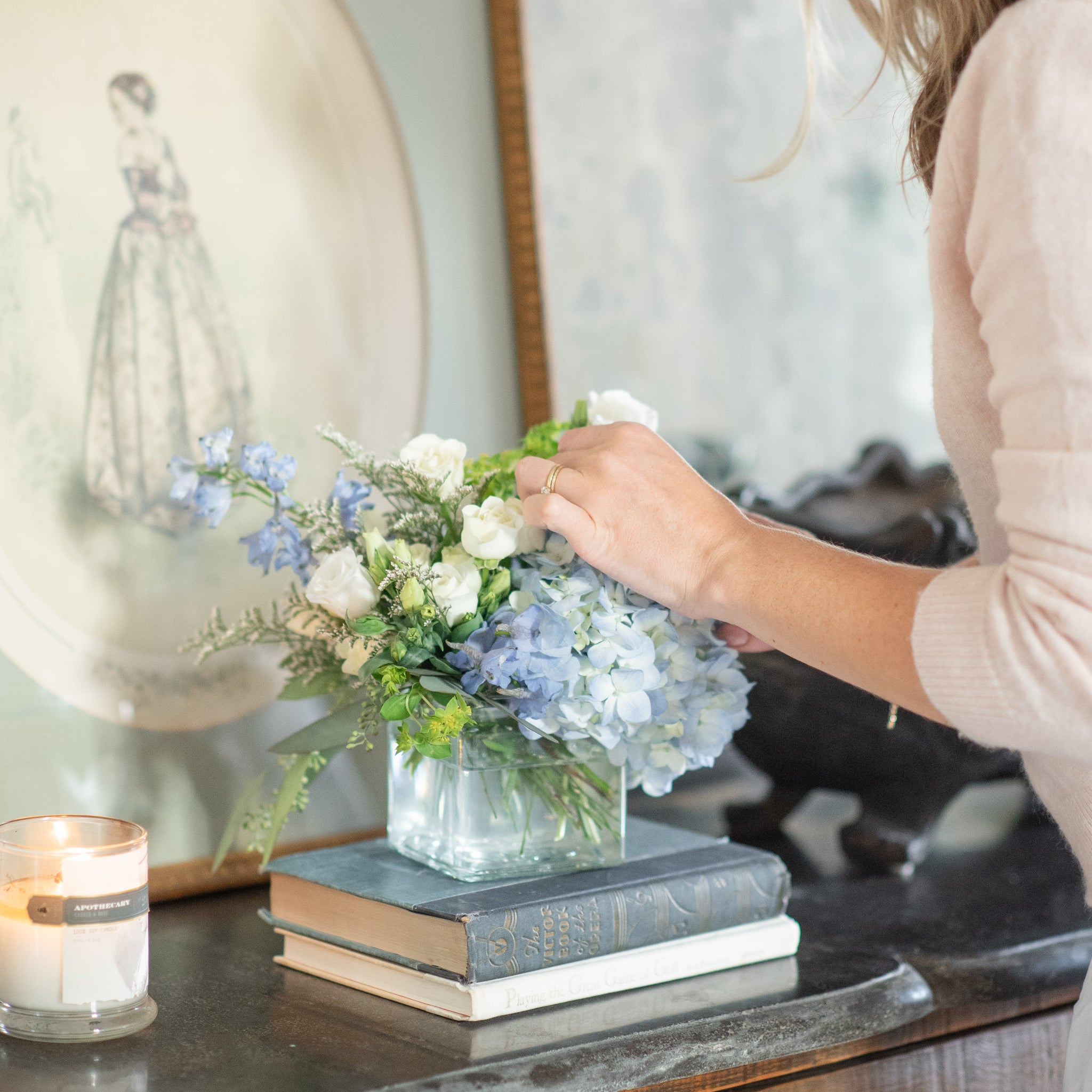 Woman arranging blue and white sympathy flowers on a table with a candle and framed picture in the background
