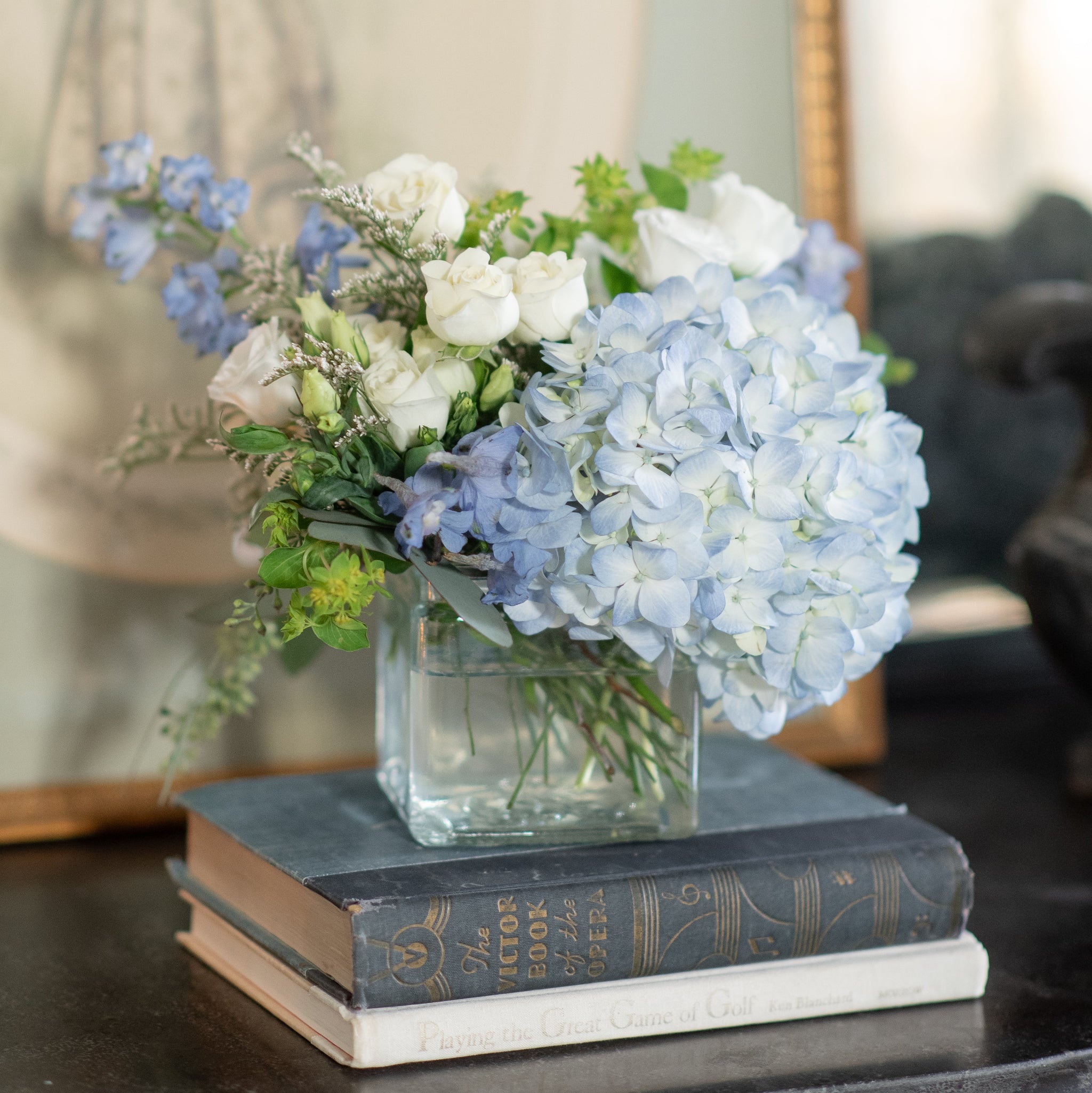 blue and white floral arrangement with delphinium, blue hydrangea, white spray roses and lisianthus on vintage books