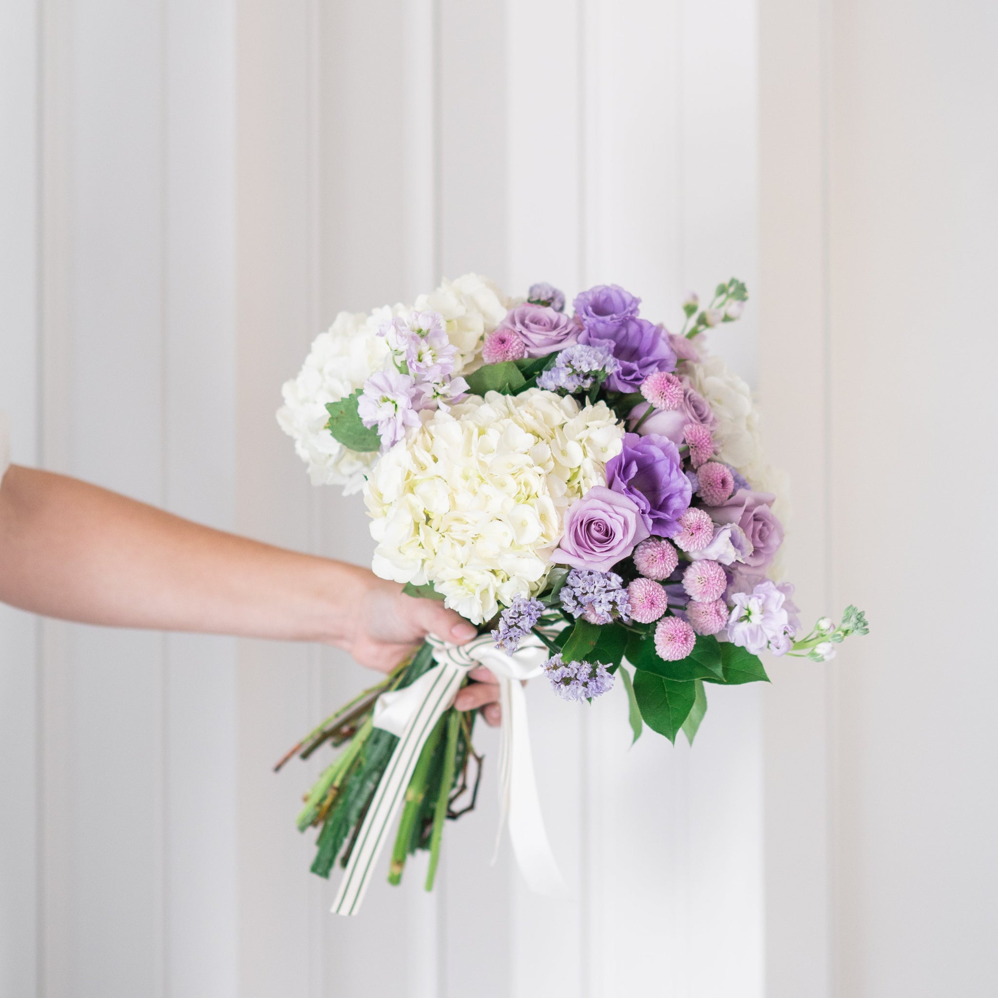 white hydrangea bouquet with pops of purple and lavender lisianthus, stock, ocean song roses. 
