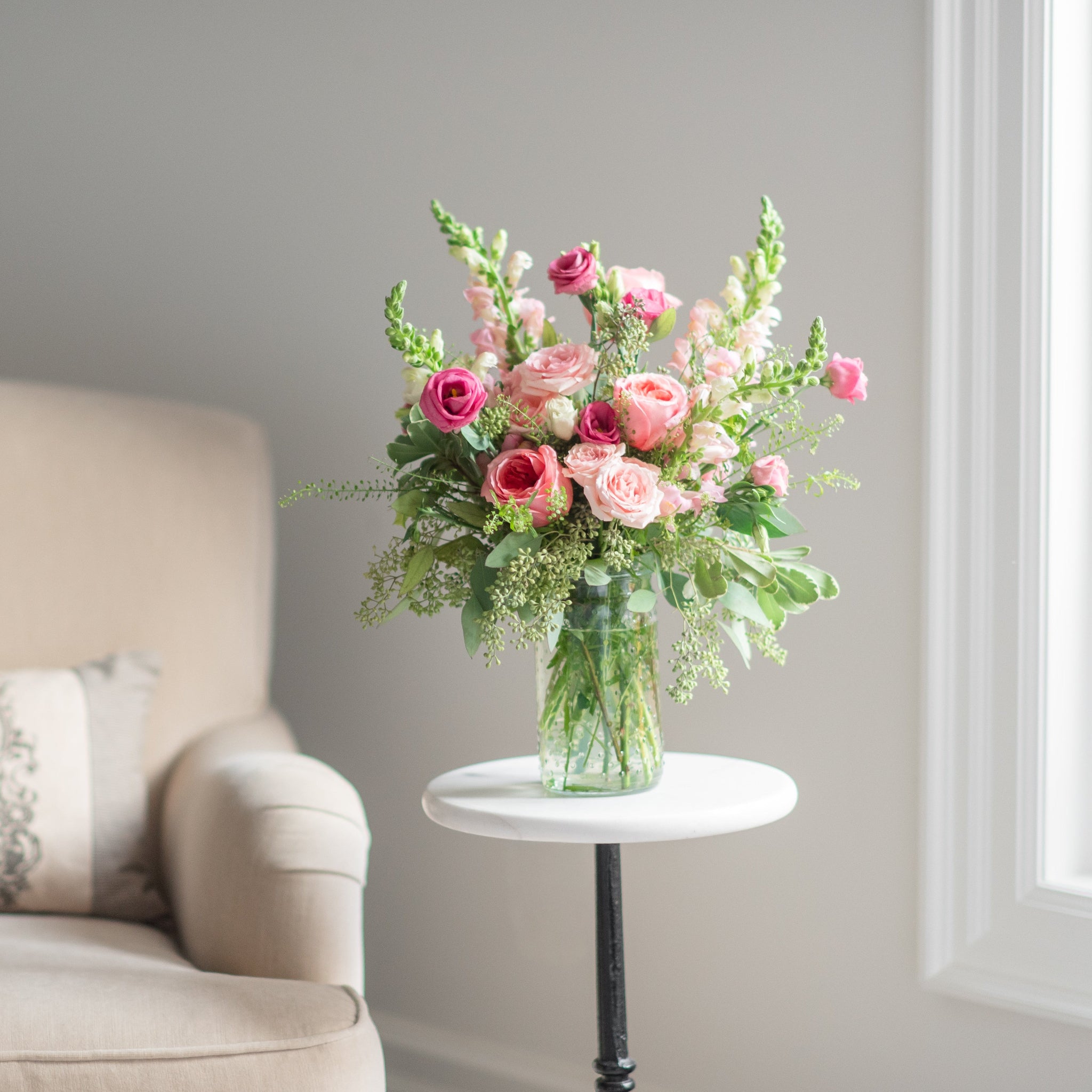 Pink floral arrangement on a small table next to a beige armchair with a decorative pillow.