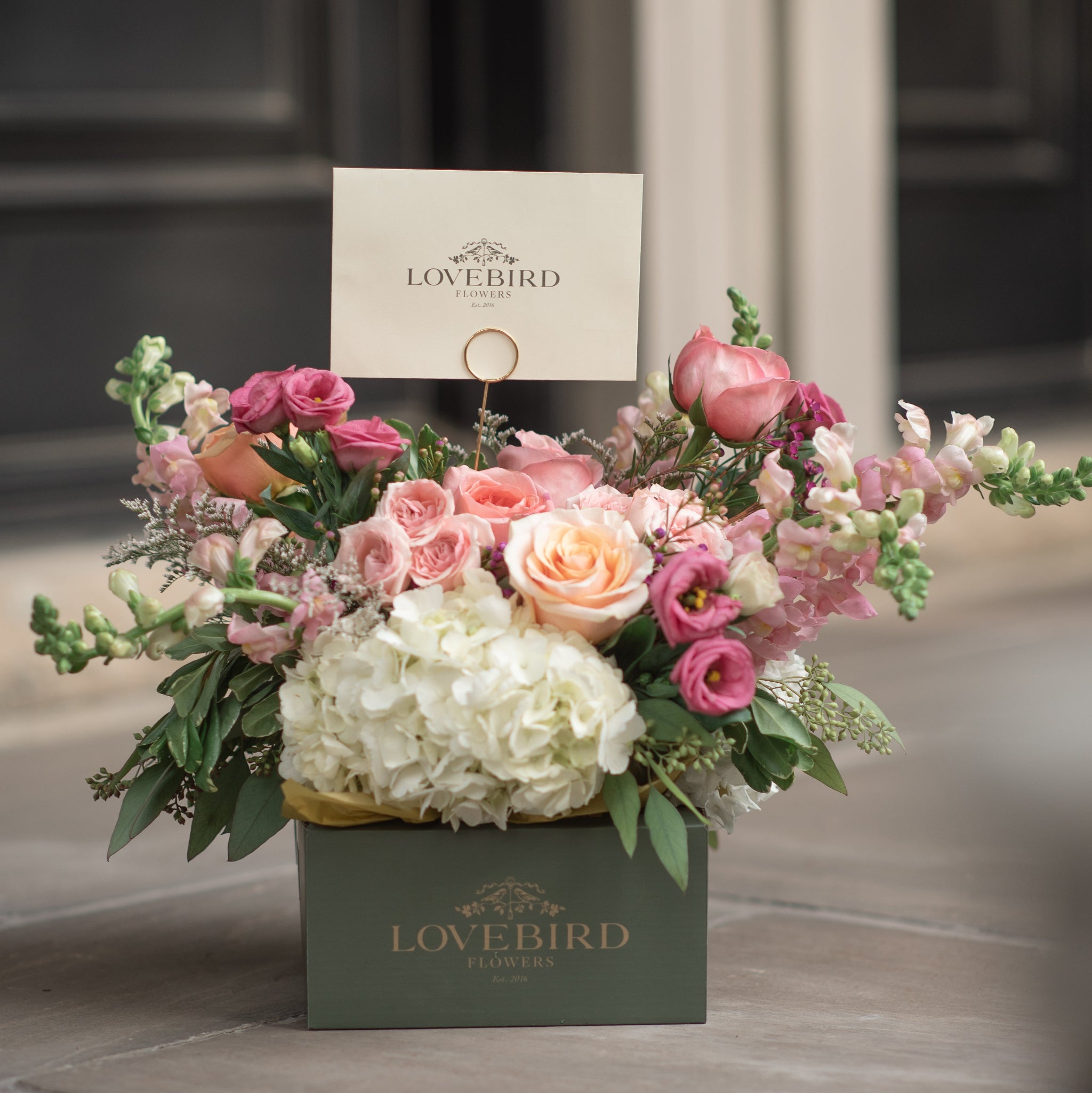 pink and peach floral arrangement with a Lovebird Flowers note card and delivery box