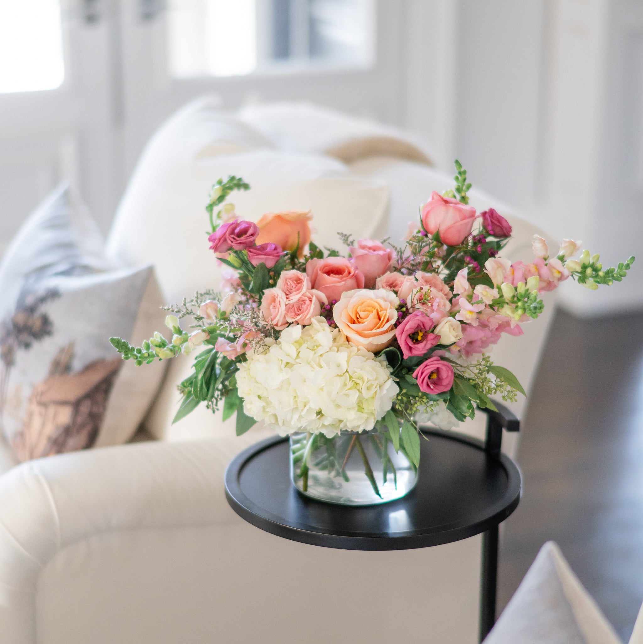pink and peach floral arrangement  in a clear jug vase on a side table 