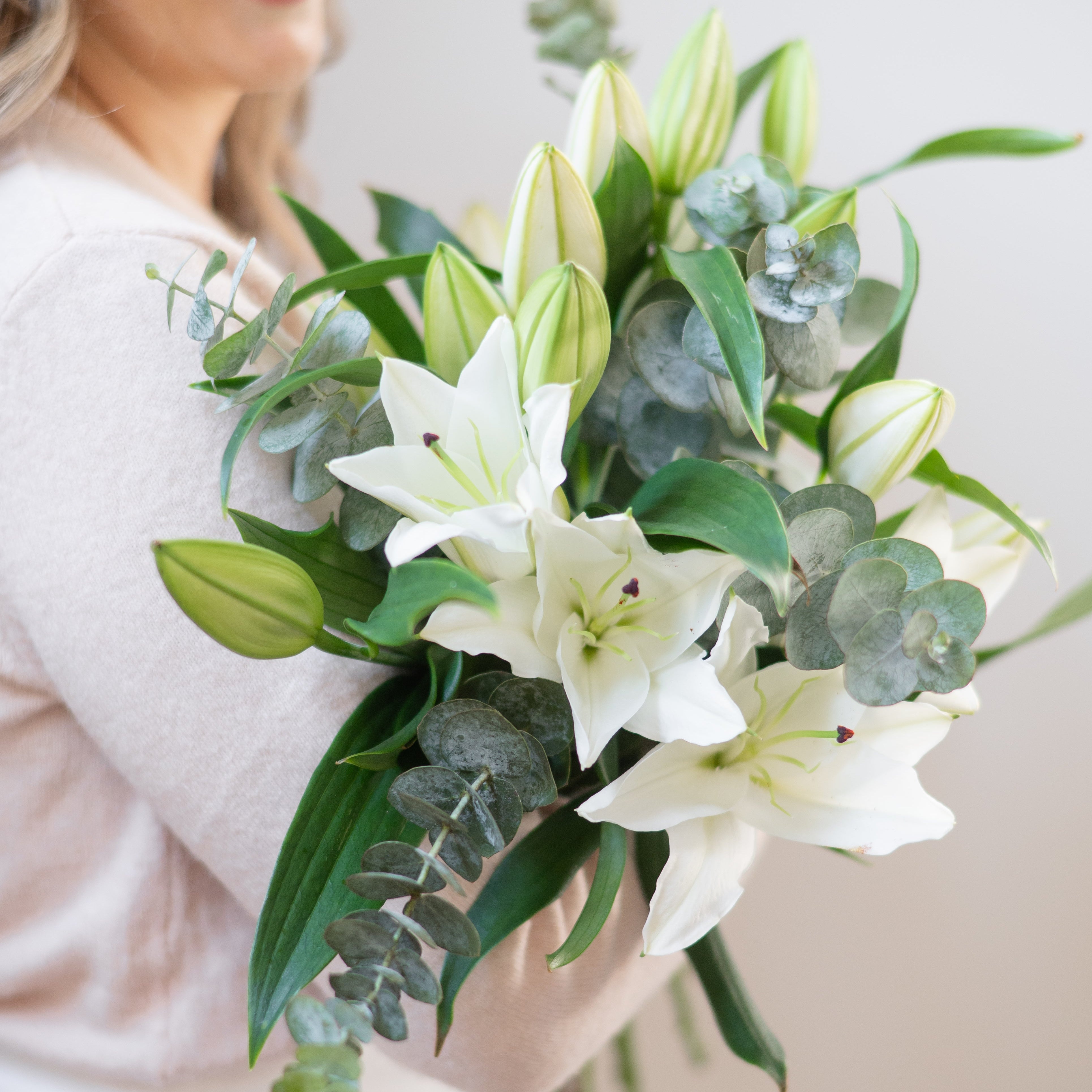 Woman holding a bouquet of white lilies and greenery against a plain background