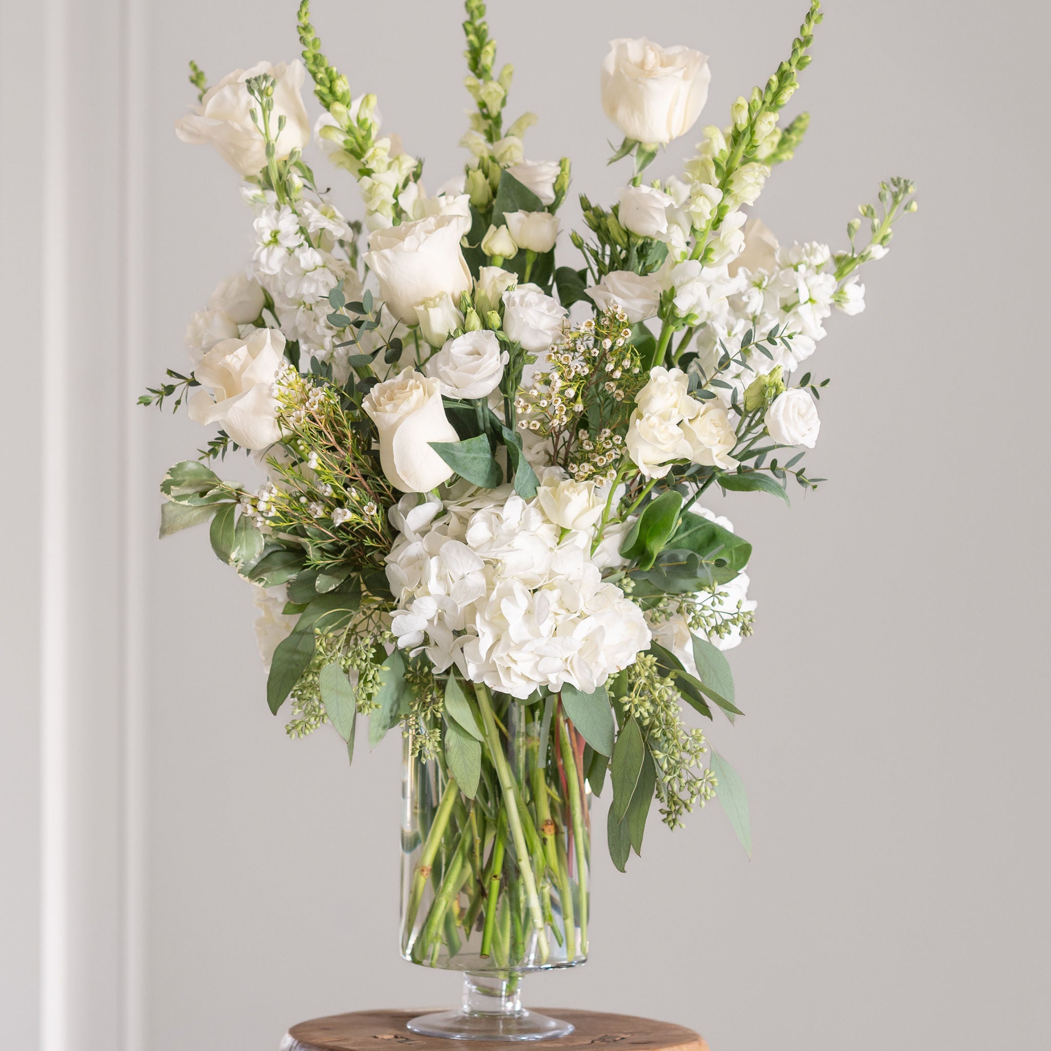 White froses, lisianthus, snap drapon, wax flower and white hydrangea towering flower arrangement in a pedestal vase