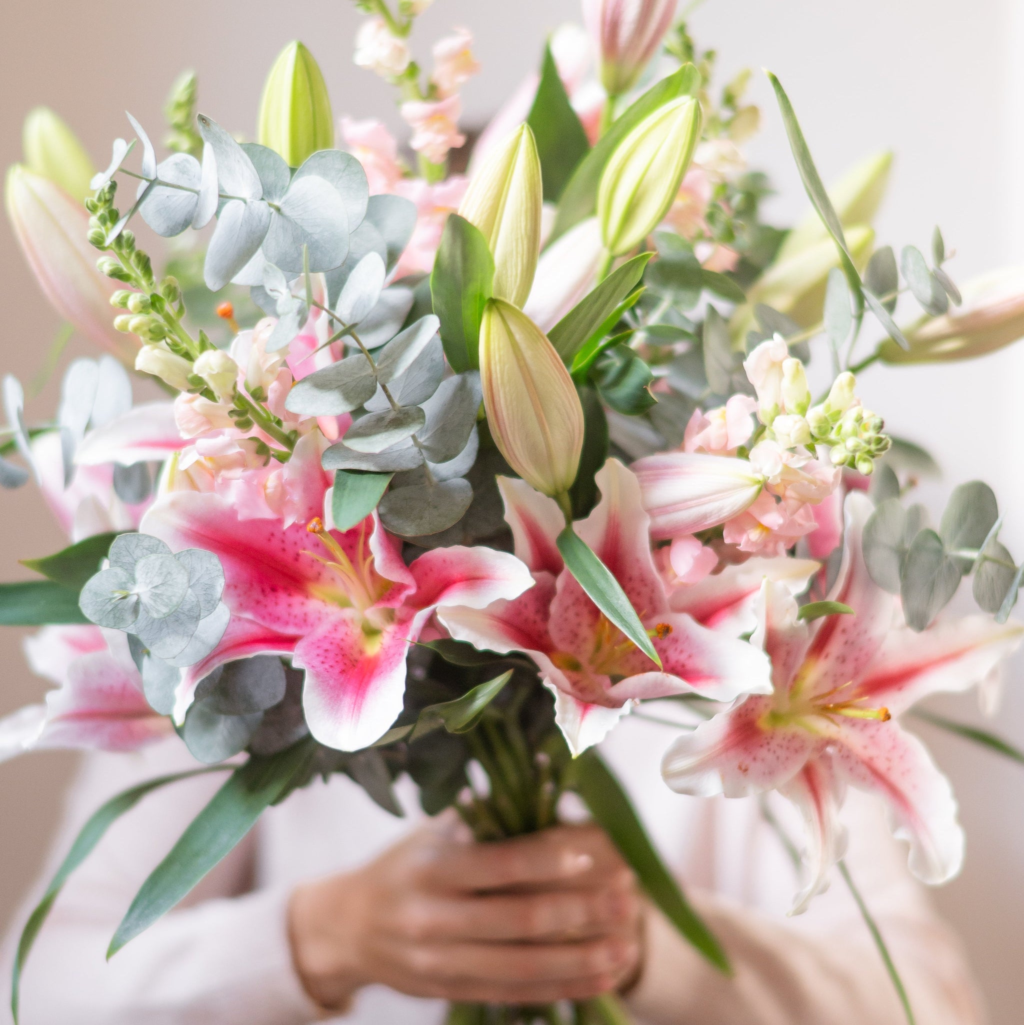 pink lilies, eucalyptus and snap dragson being held