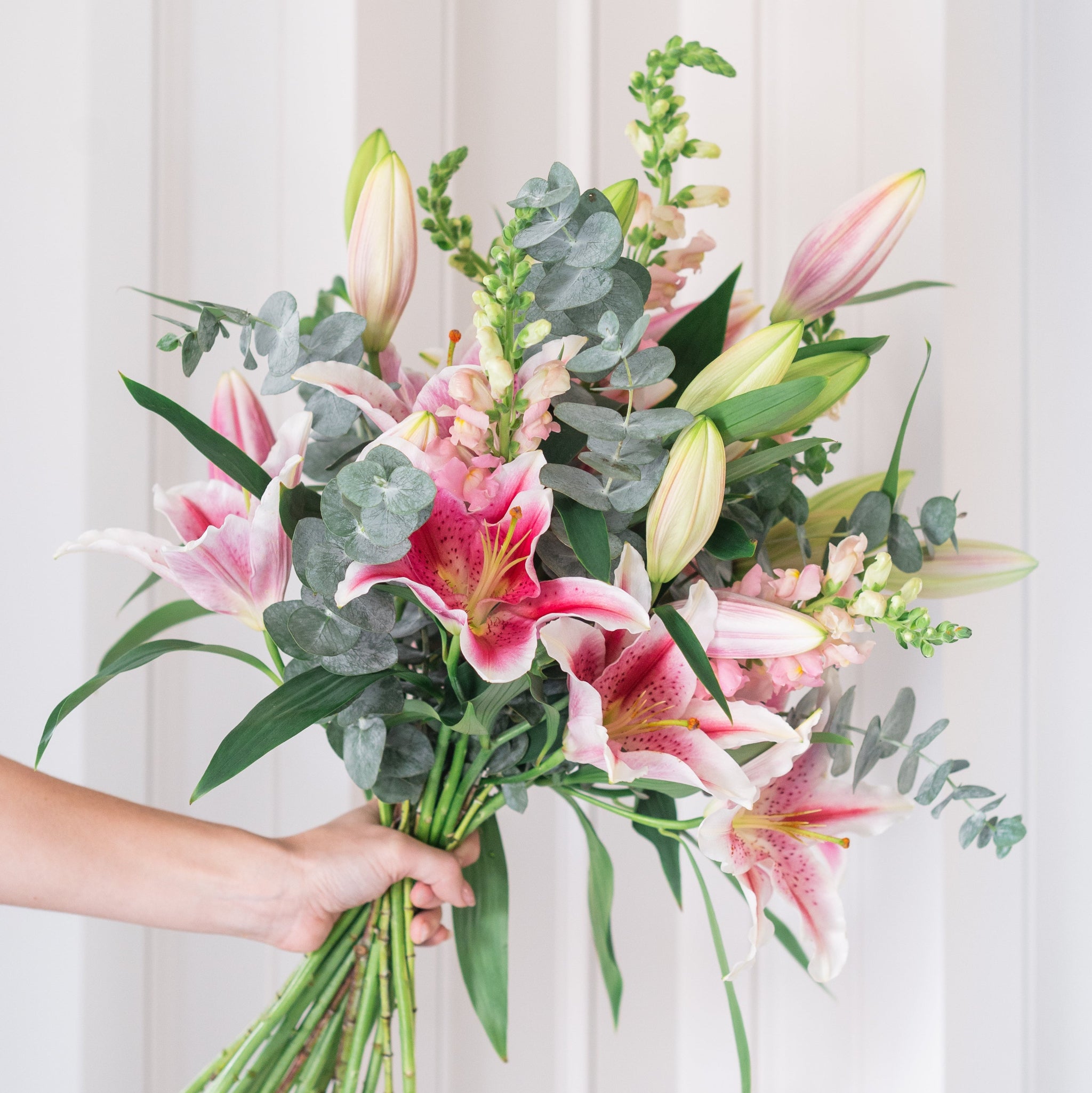Bouquet of pink and white flowers held by a hand against a white door background
