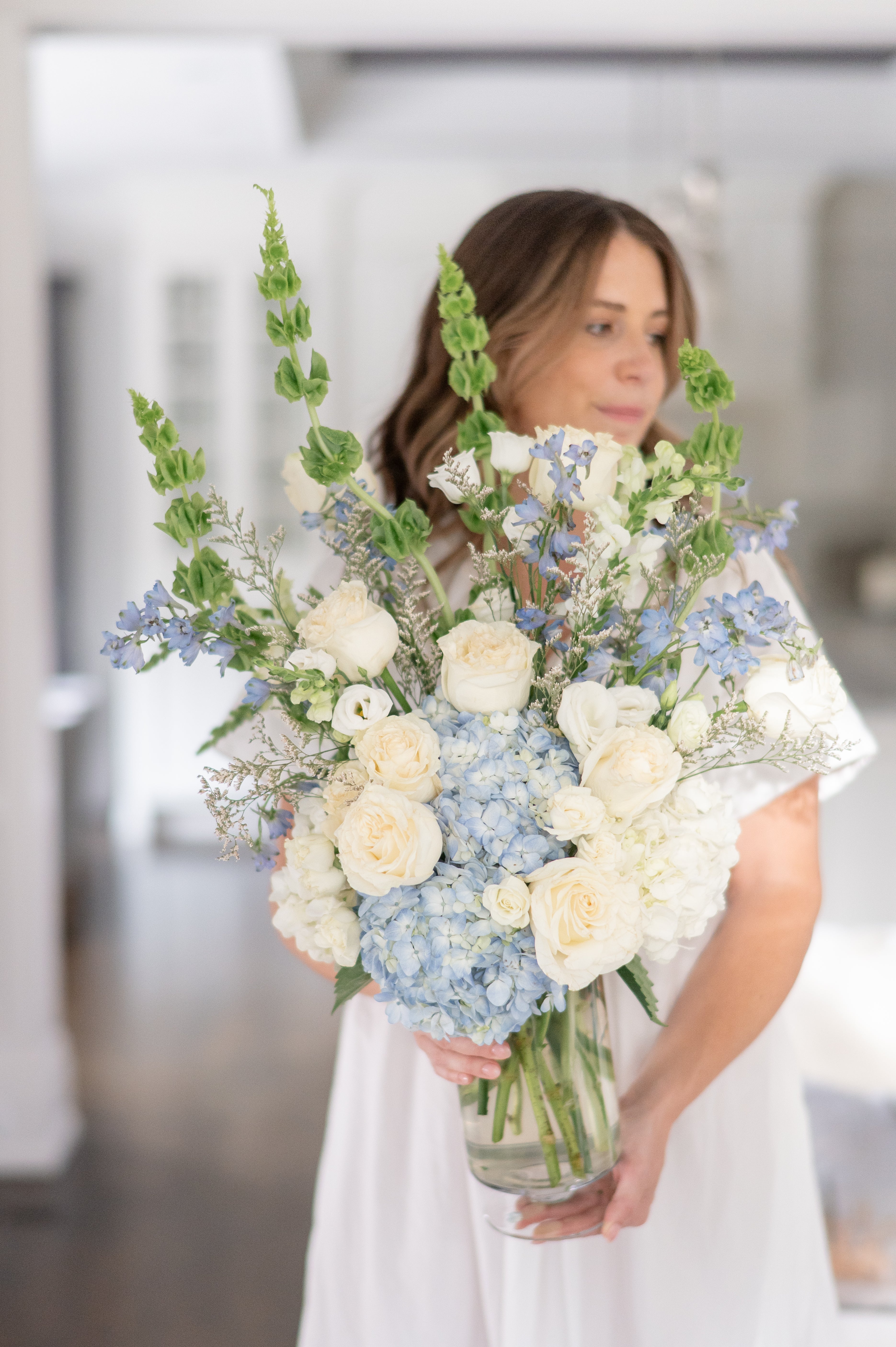 Woman holding a large arrangement of blue and white hydrangeas, bells of ireland and delphinium for a funeral