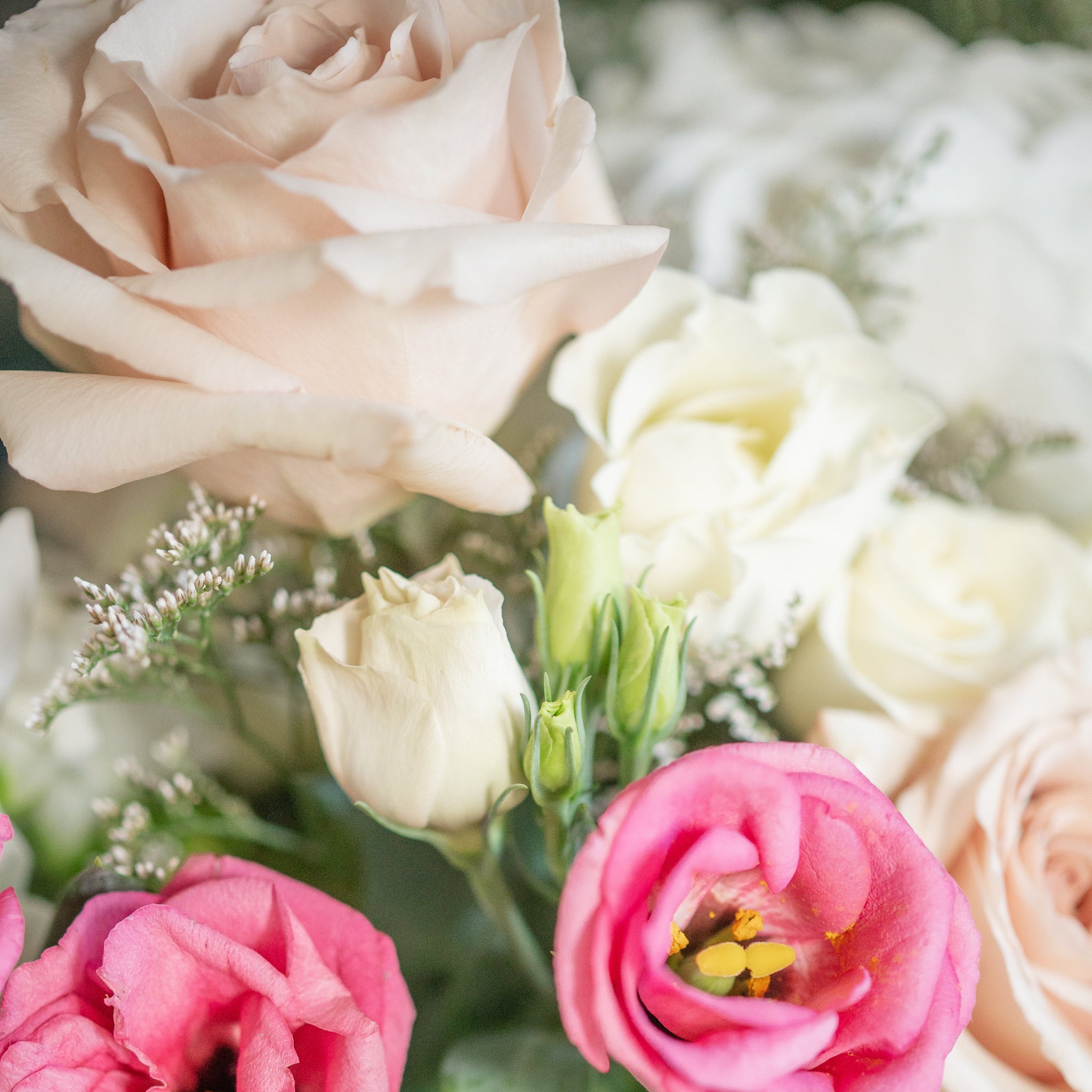 Close-up of a bouquet of pink, lisianthus,b blush quicksand roses, white spray roses with greenery.