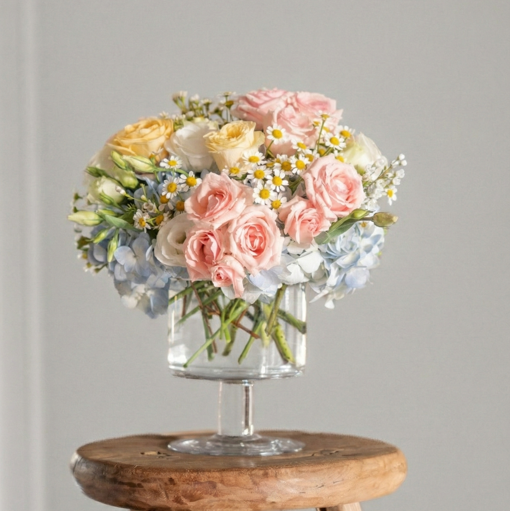 Bouquet of flowers in a clear vase on a wooden stool against a gray wall