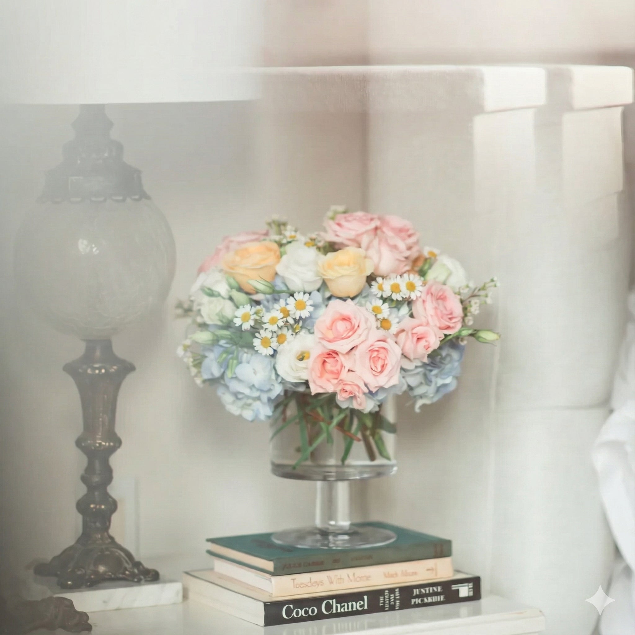 pastel flower arrangement with feverfew, buttercup roses, blush roses and blue hydrangea on vintage books